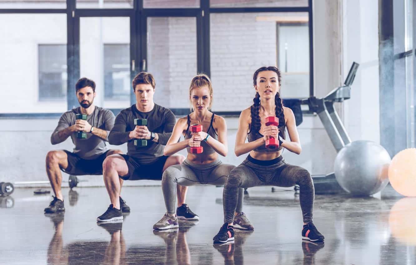 Dumbbell 桌布 壁紙 — 四位體態健美的人在一個明亮現代、地板反光且有大窗戶的健身房用啞鈴做深蹲運動。