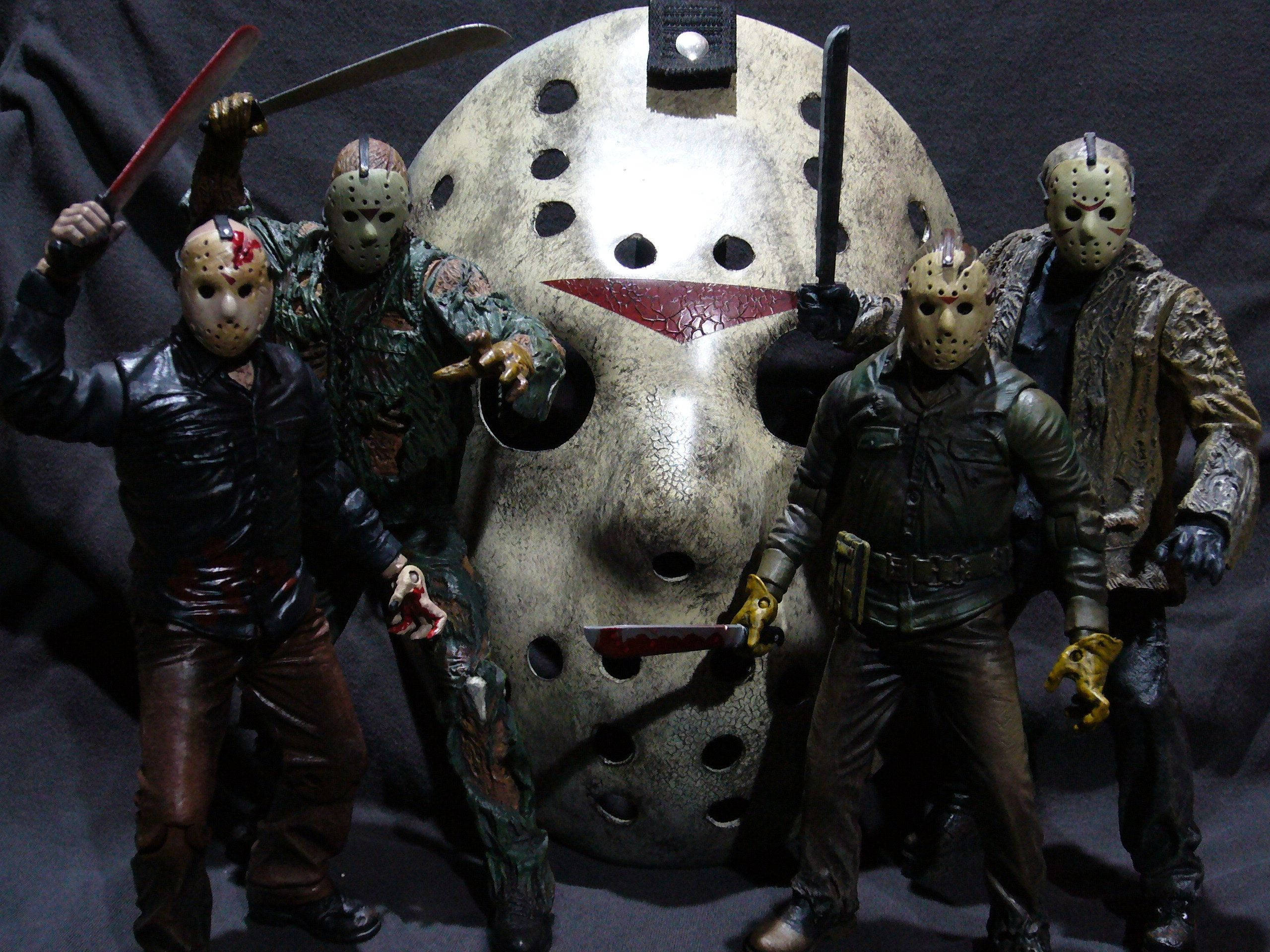 Friday 桌布 壁紙 — 四個 Jason Voorhees 動作人偶，戴著血跡斑斑的面具和拿著刀，在黑暗背景下圍繞一個巨大的曲棍球面具擺出威脅姿勢。