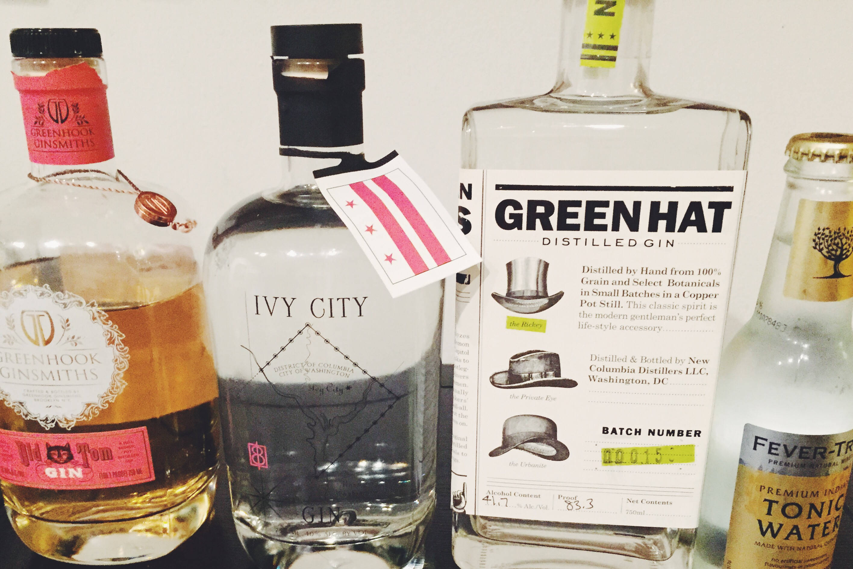 Gin 桌布 壁紙 — 四個不同的酒瓶，包括琴酒和通寧水，整齊地排列在深色表面上，背景是純白色的牆壁。