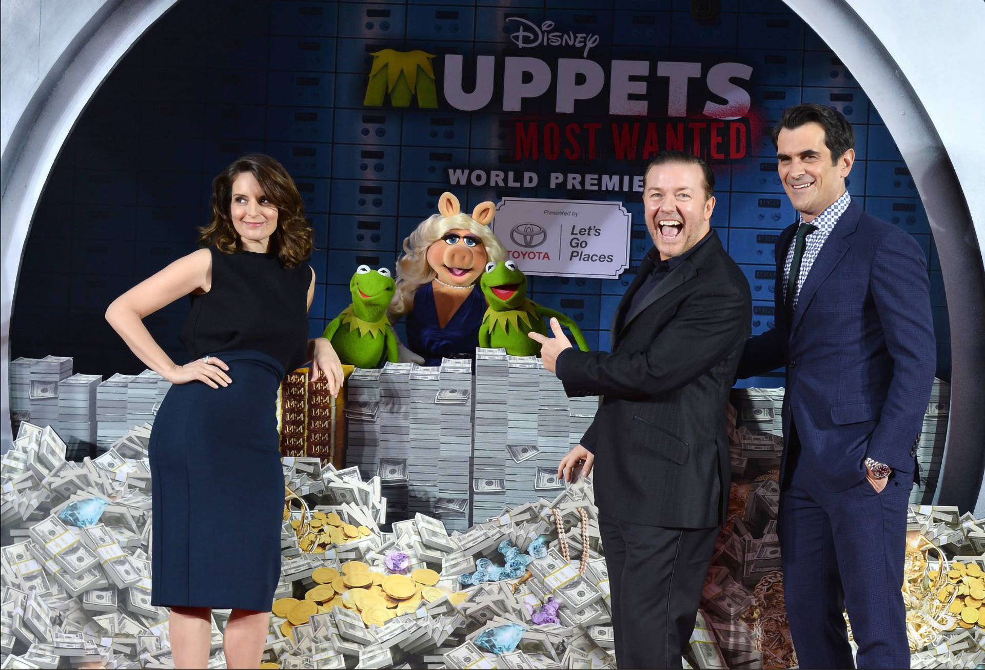 muppets 桌布 壁紙 — 四個人和兩個 Muppet 角色在電影首映活動中愉快地站在一堆現金上擺姿勢。