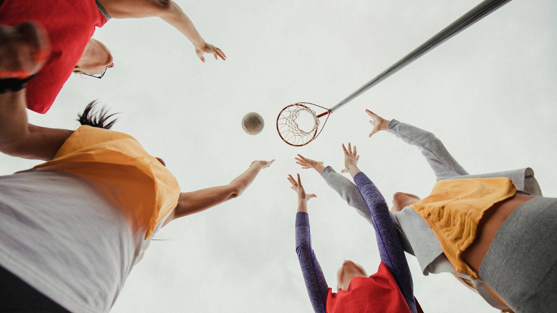 ball 桌布 壁紙 — 四個人從下方躍起，雙臂伸向籃框上方空中的籃球，背景為多雲的天空。