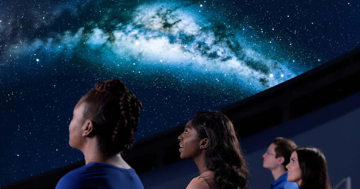 Planetarium 桌布 壁紙 — 四個人抬頭敬畏地看著黑暗天花板上令人驚嘆的銀河系投影。