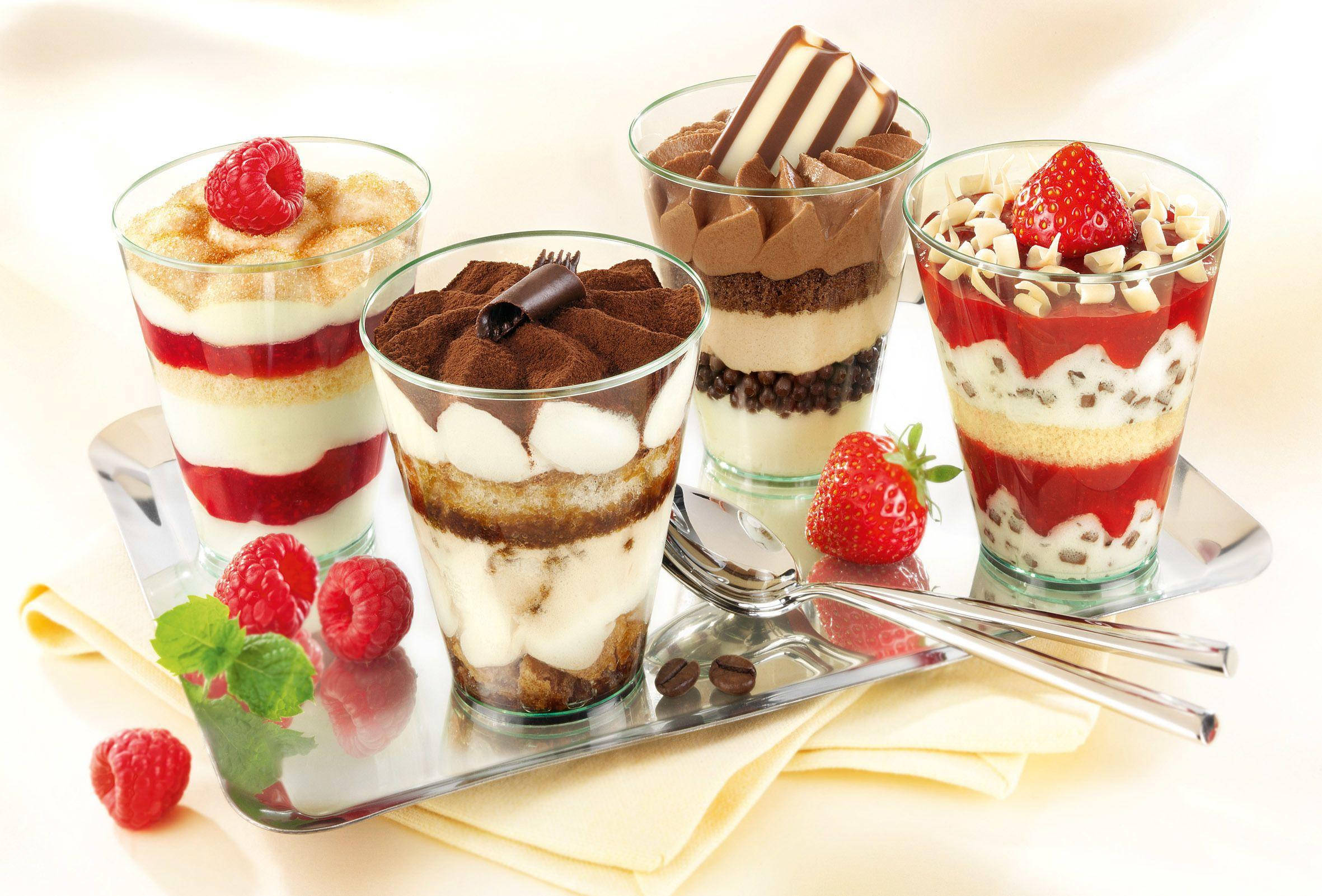 Yogurt 桌布 壁紙 — 四個優雅玻璃杯裝滿層層提拉米蘇甜點，上面放上新鮮莓果和巧克力裝飾。