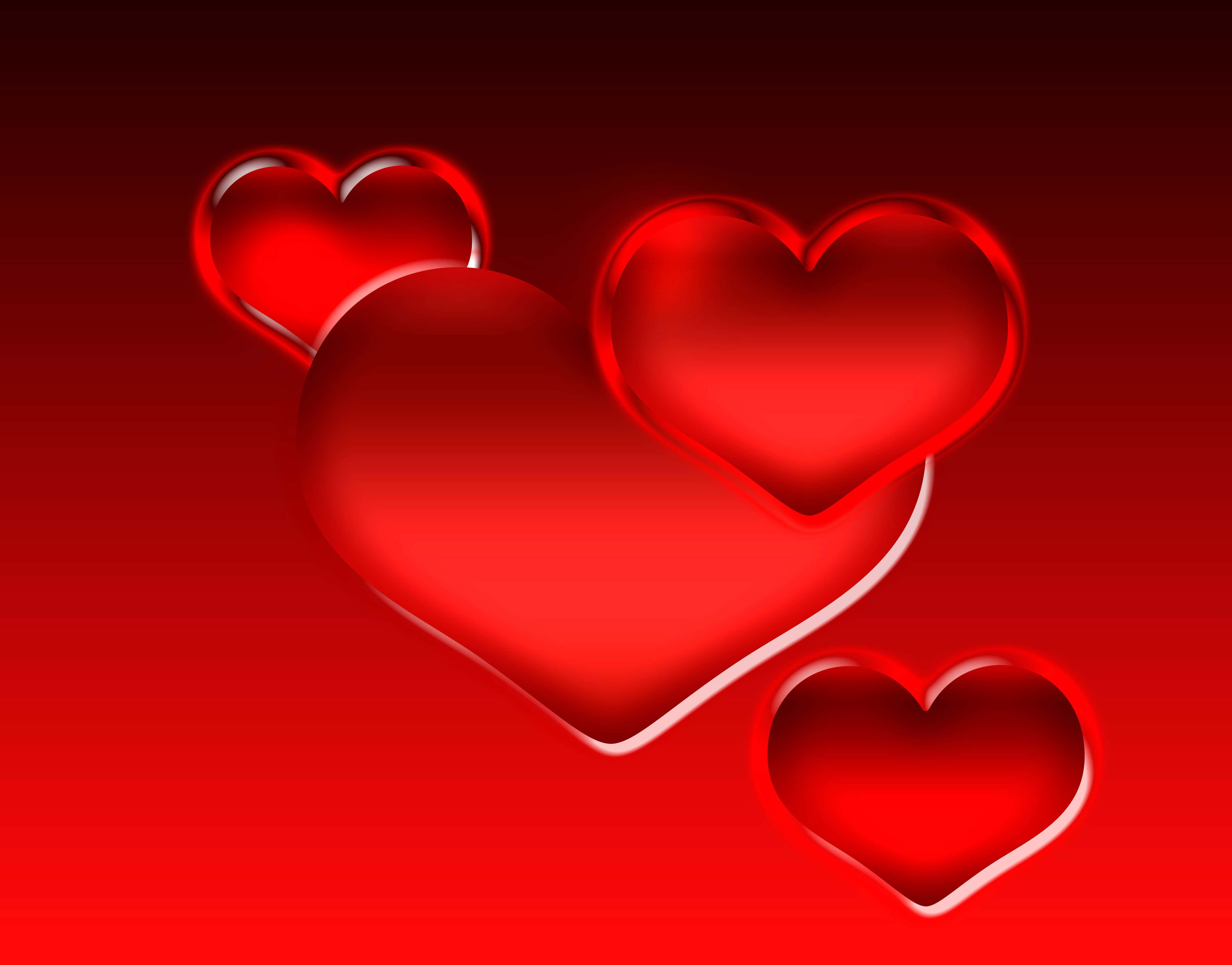 Red Heart 桌布 壁紙 — 四個光滑的紅色心形漂浮在帶有柔和高光的漸變紅色背景上。