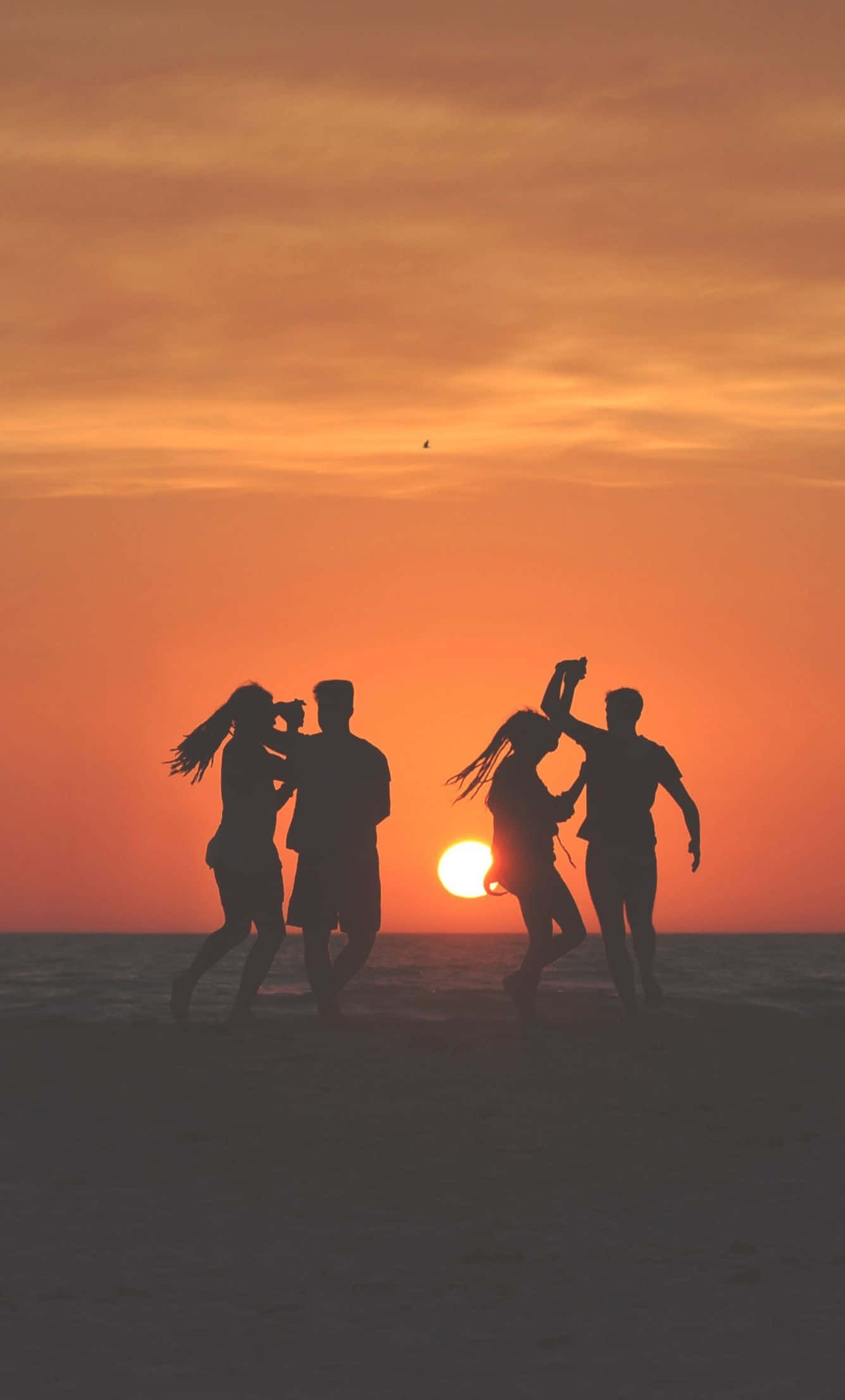 Beach Dance Party 桌布 壁紙 — 四個剪影朋友在沙灘上歡快地跳舞，夕陽呈現火熱的橙色和粉紅色調。