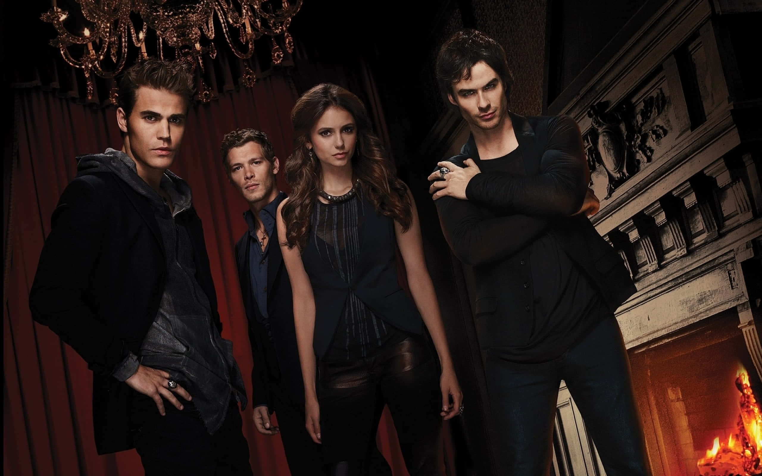 Vampire Diaries Desktop 桌布 壁紙 — 四個吸血鬼在一個哥德式大宅中戲劇性地擺姿勢，背景有熊熊燃燒的壁爐和華麗的水晶吊燈。