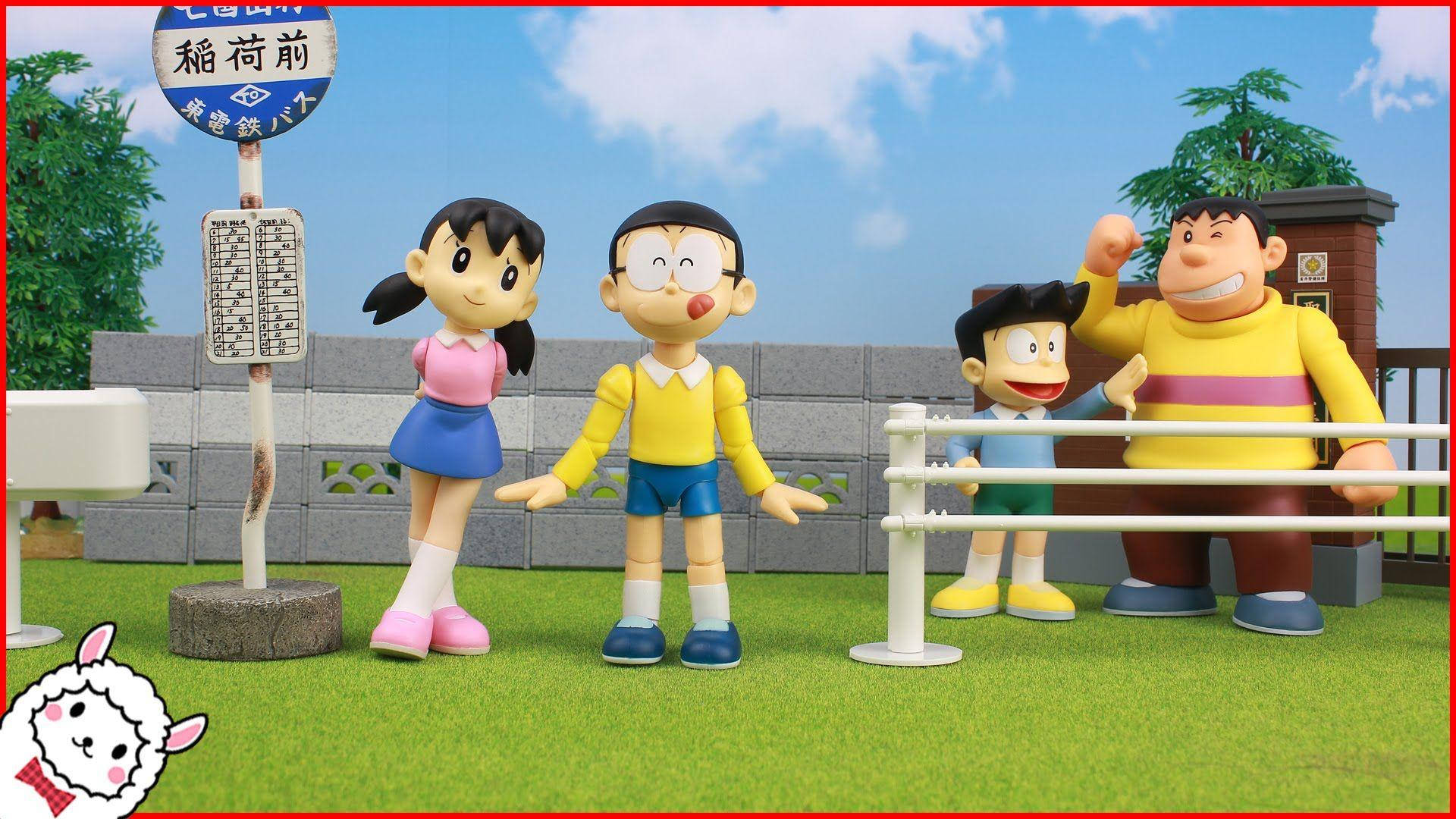 Doraemon 桌布 壁紙 — 四個哆啦A夢角色站在草地上，靠近一個日本火車站標誌，背景是明亮的藍天。