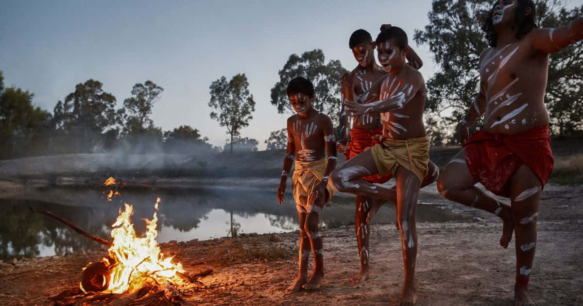 Aboriginal 桌布 壁紙 — 四個塗上白色身體彩繪的小孩在黃昏時分，於霧氣瀰漫的水坑附近，圍著發光的營火快樂地跳舞。