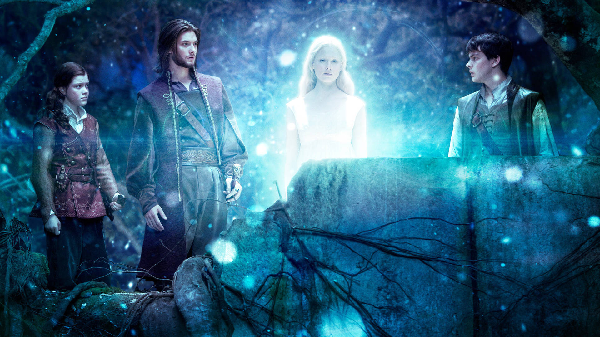 Narnia 桌布 壁紙 — 四個奇幻角色站在一個散發藍光和漂浮粒子的神秘森林中。