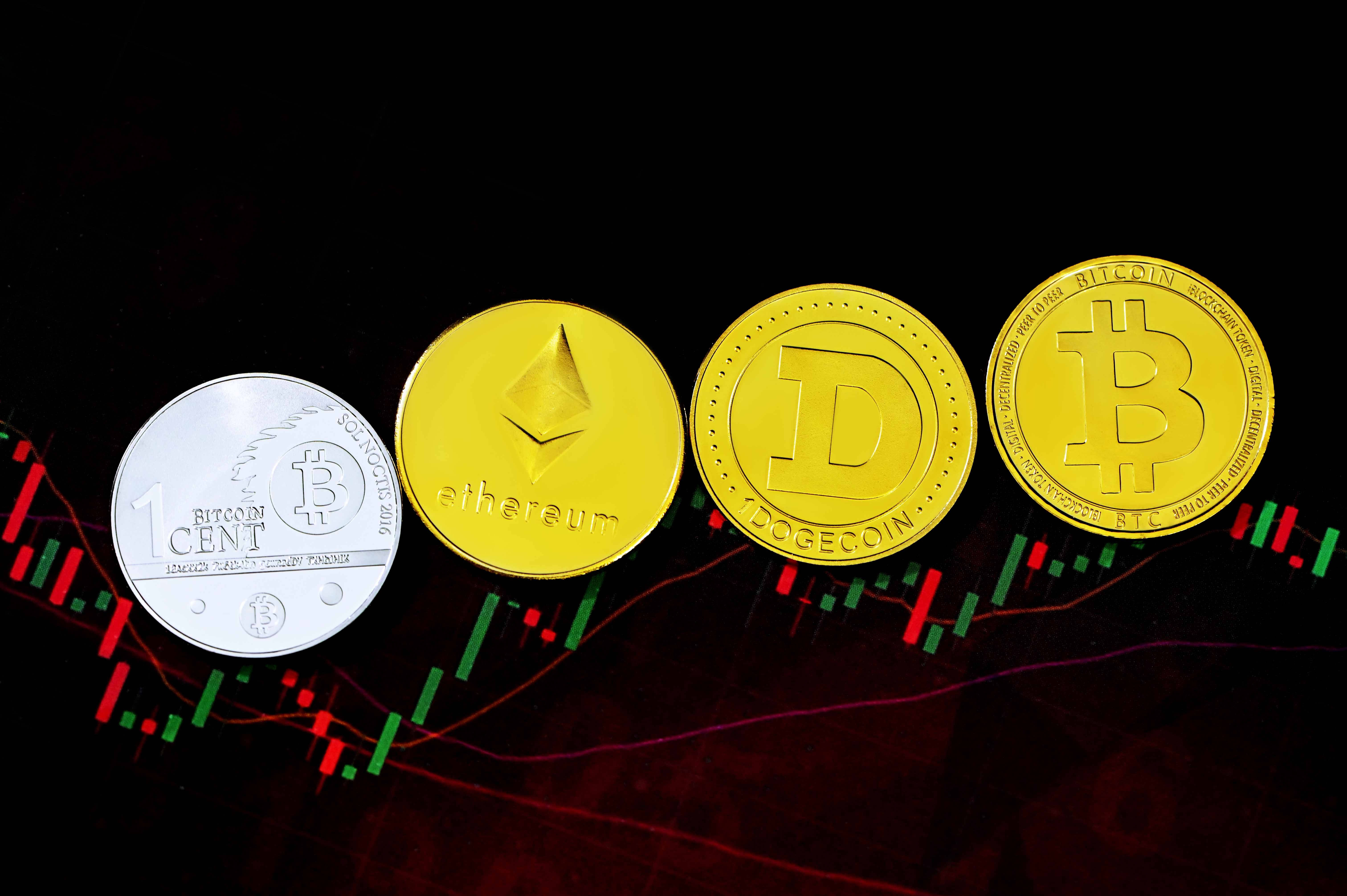 Dogecoin 桌布 壁紙 — 四個實體加密貨幣硬幣 Bitcoin Ethereum Dogecoin 和一個銀色 Bitcoin 仙硬幣放在一個發光的股票圖表上，帶有紅色和綠色條形。