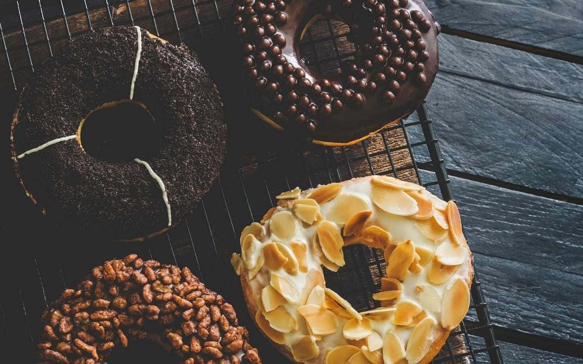 Pastry 桌布 壁紙 — 四個巧克力糖霜杏仁和彩針裝飾的頹廢甜甜圈放在深色木面上的金屬架上。