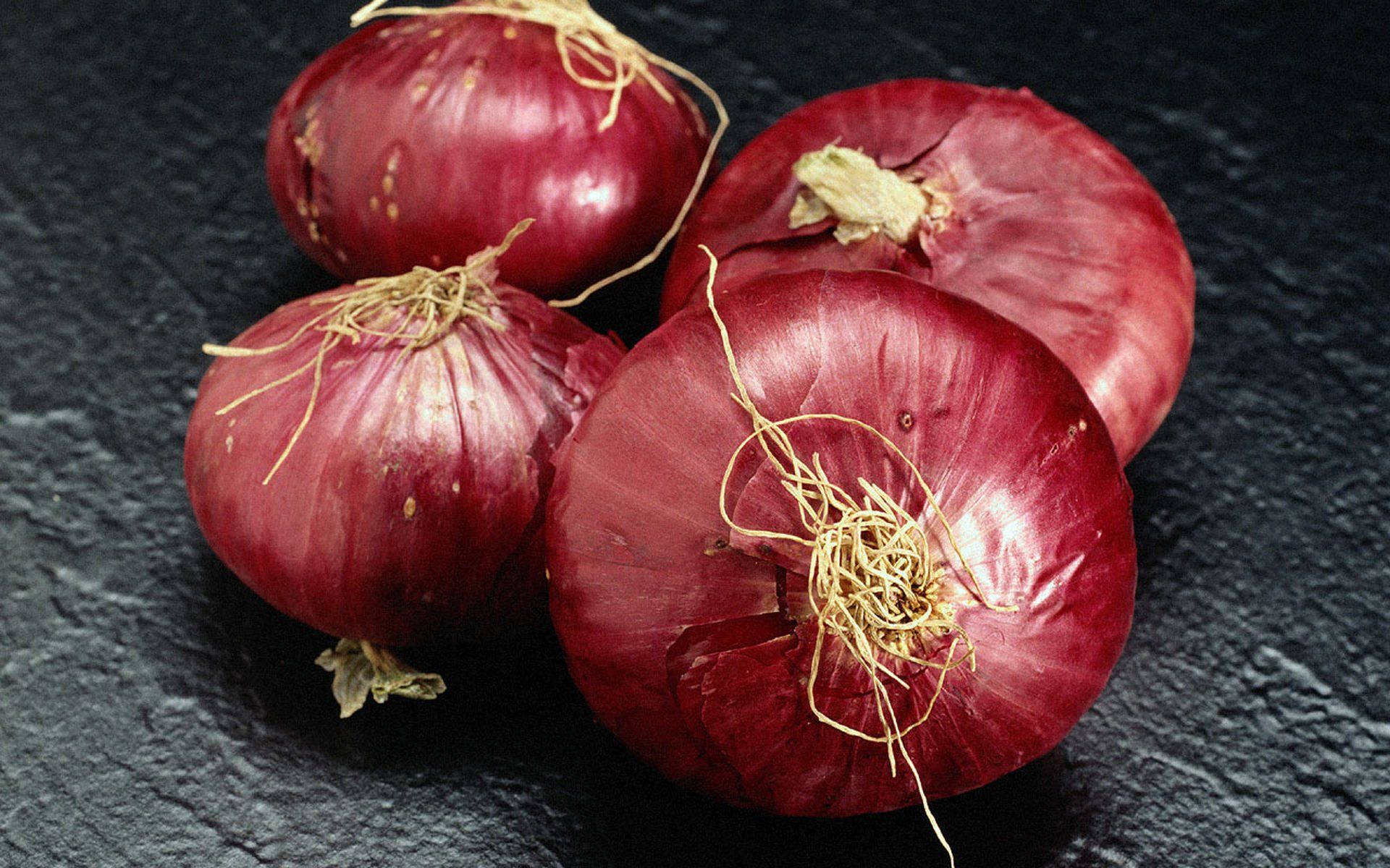 Onion 桌布 壁紙 — 四個帶有乾燥根部的光澤紅洋蔥，放置在深色紋理板岩表面上。