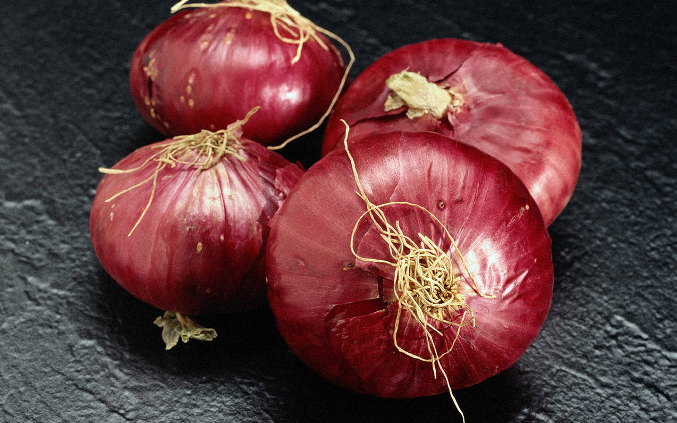 Onion 桌布 壁紙 — 四個帶有乾燥根部的光澤紅洋蔥，放置在深色紋理石板表面上。