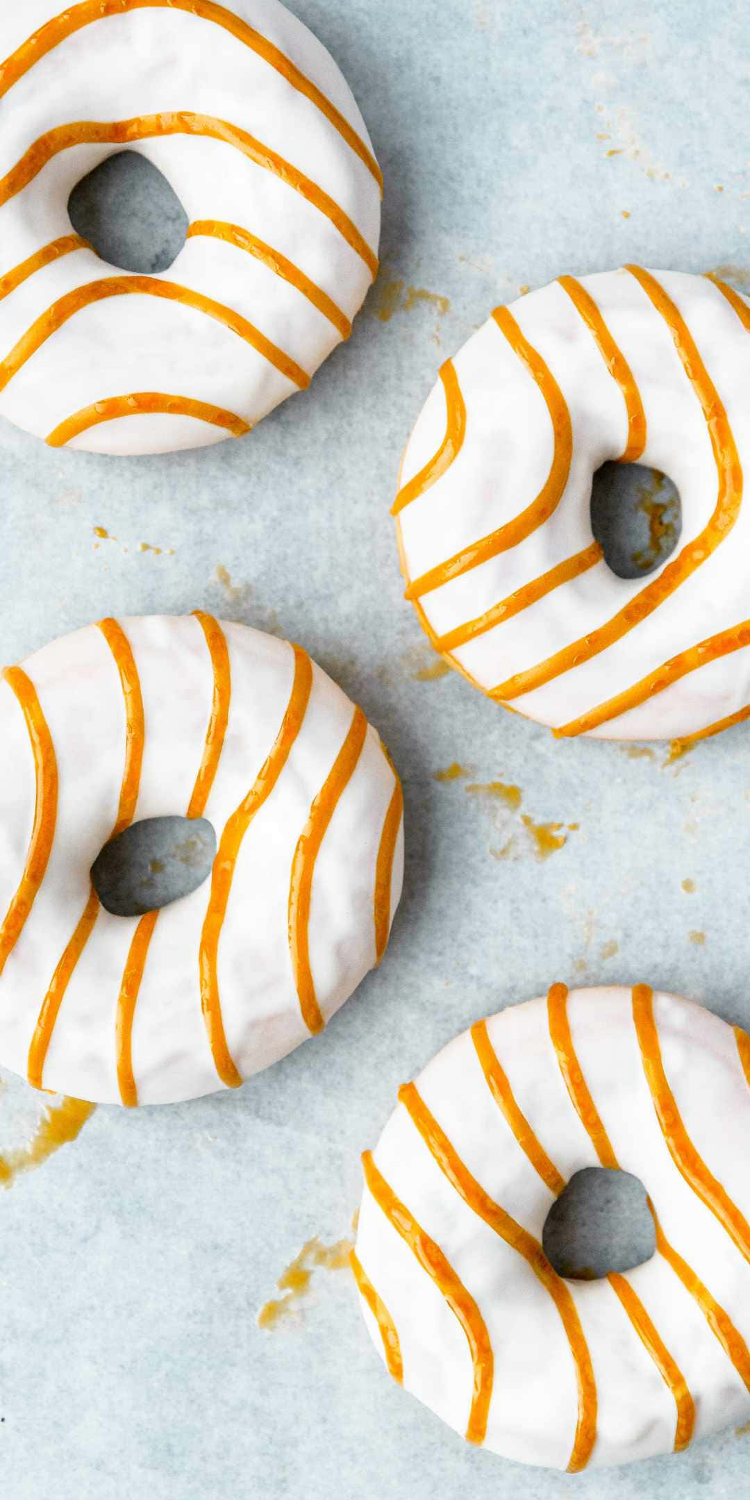 Pastries 桌布 壁紙 — 四個帶有橙色條紋的釉面甜甜圈放在淺藍色表面上，周圍散落著碎屑。