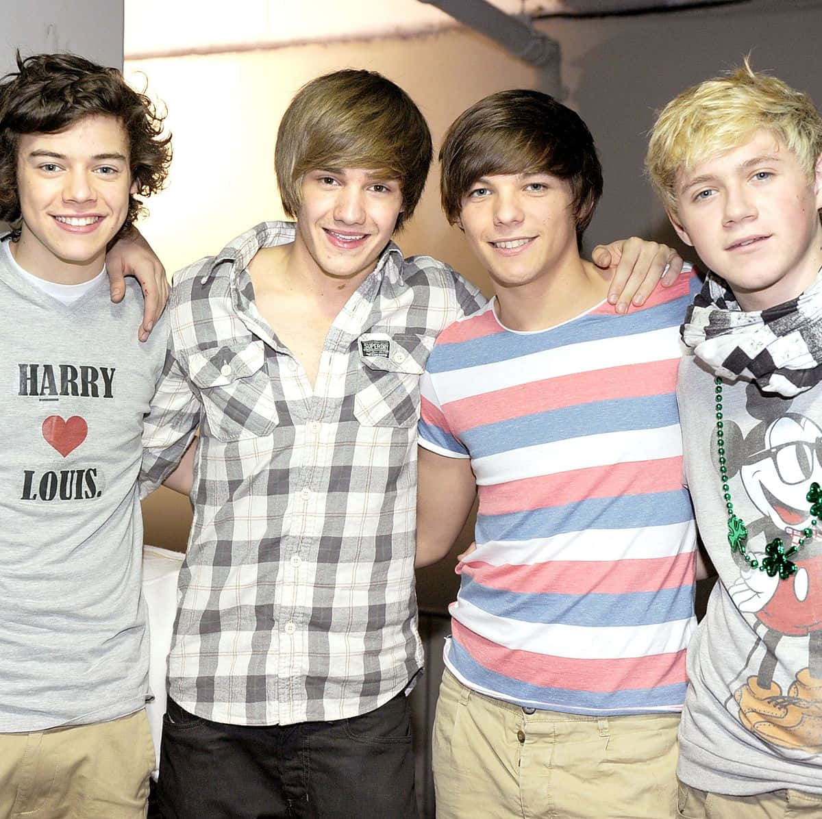 One Direction 桌布 壁紙 — 四個年輕男子互相搭著肩膀，穿著休閒服裝，在純色背景前燦爛微笑。