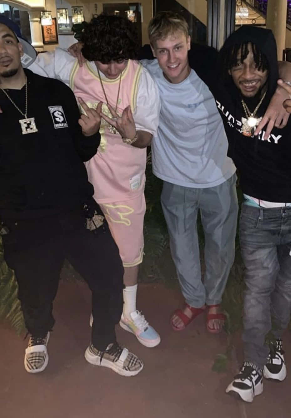 Shoreline Mafia 桌布 壁紙 — 四個年輕男子在夜間於溫暖照明的室內空間一起擺姿勢，微笑並做手勢。