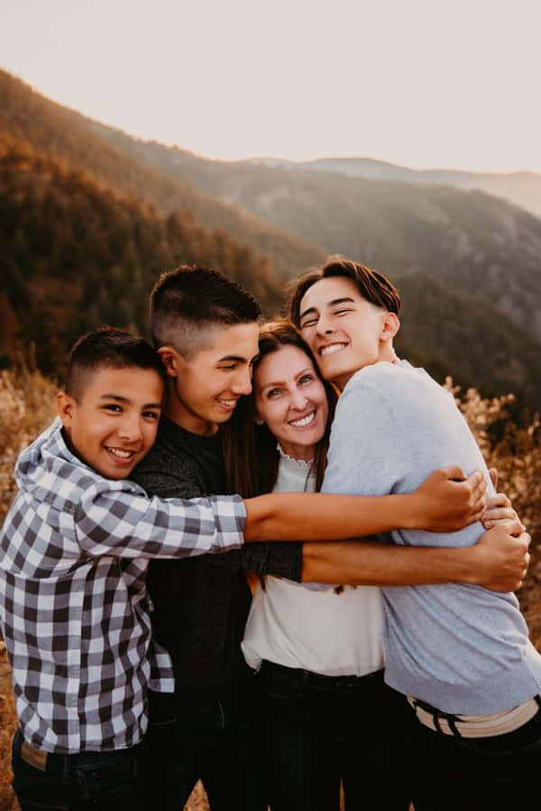 Family Portrait 桌布 壁紙 — 四個微笑的人在金色日落山景背景下溫暖地擁抱。