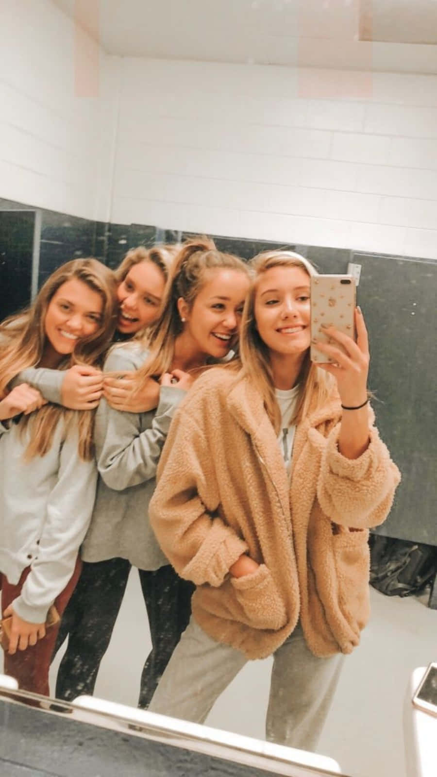 Friendship 桌布 壁紙 — 四個微笑的年輕女性穿著舒適的抓絨外套和運動褲，在鏡子自拍中緊靠在一起。
