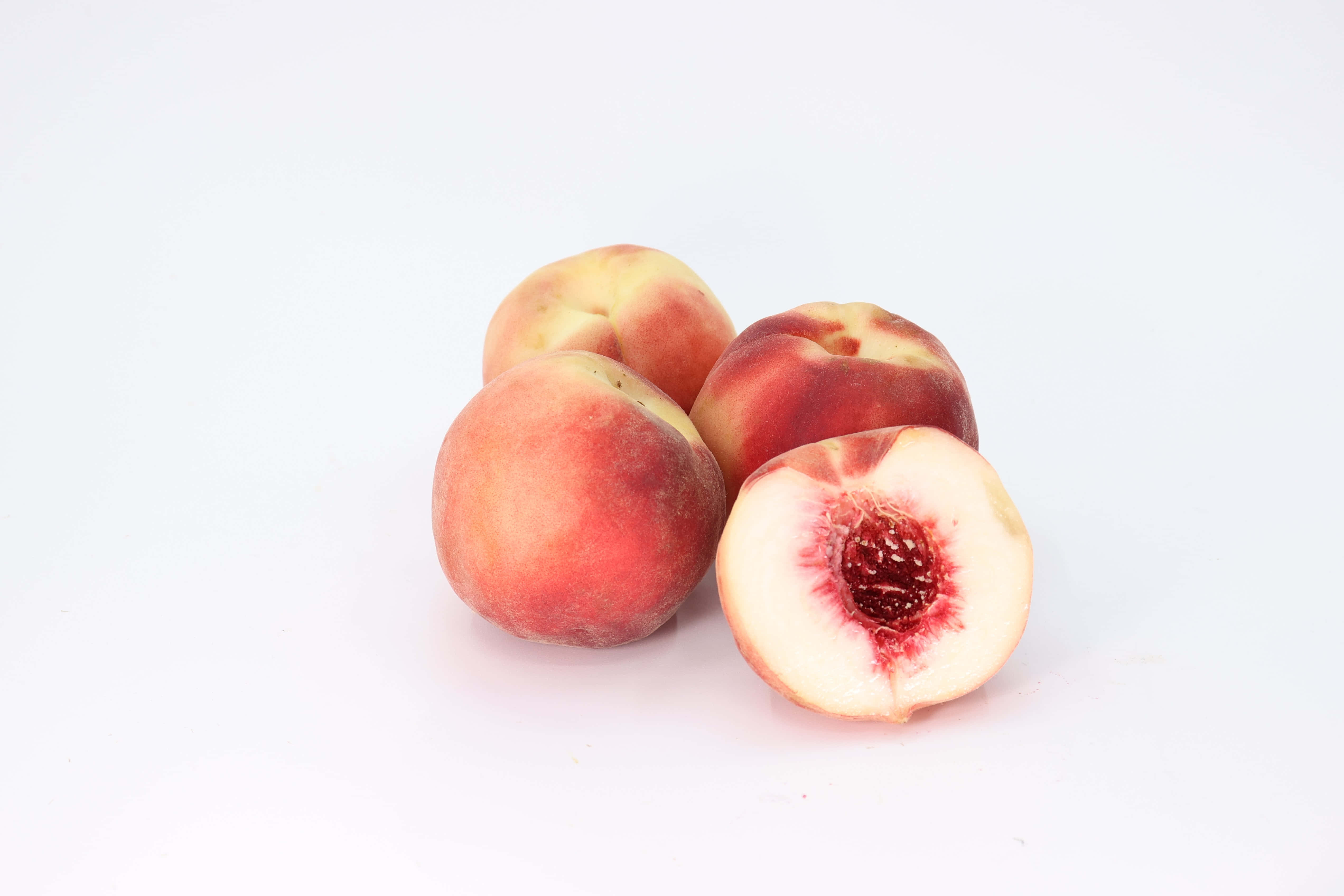 Peaches 桌布 壁紙 — 四個成熟的桃子，其中一個切開，露出多汁的紅色果肉，背景是乾淨的白色。