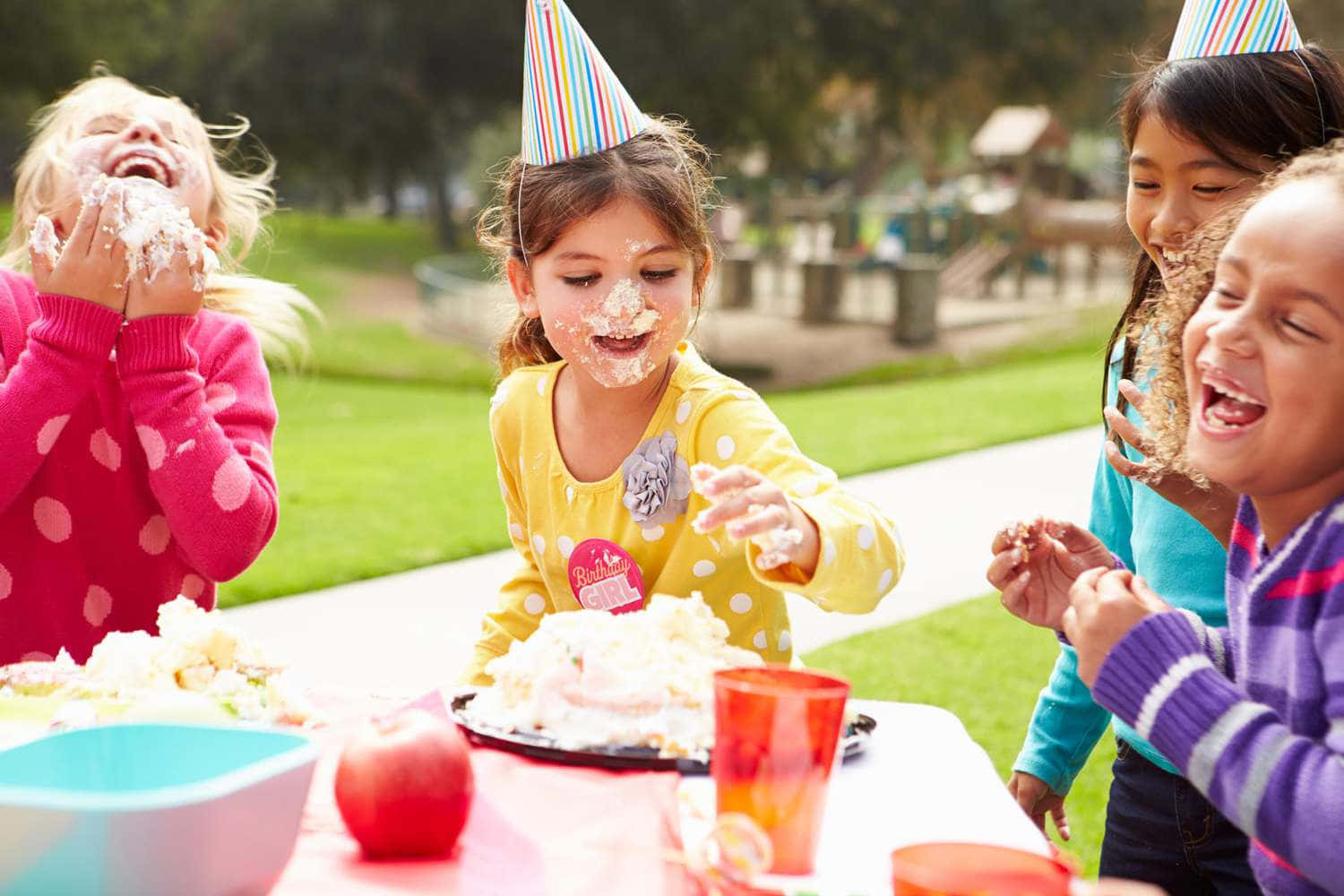 Party 桌布 壁紙 — 四個戴著派對帽的快樂孩子在戶外生日野餐中笑著互相塗抹糖霜。