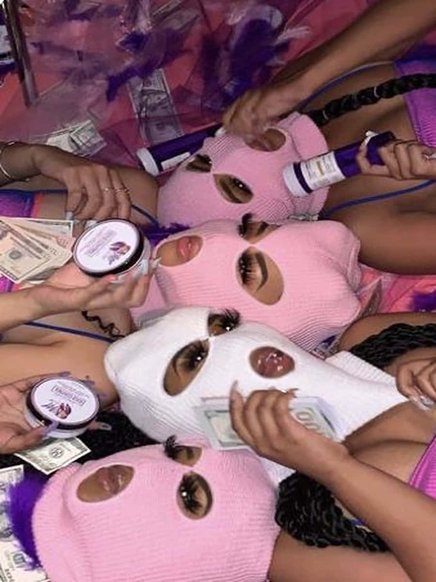 Ski Mask Girl 桌布 壁紙 — 四個戴著粉紅色和白色巴拉克拉瓦頭套的人，在充滿活力的紫色環境中，在散落的現金和美容產品之間閒逛。