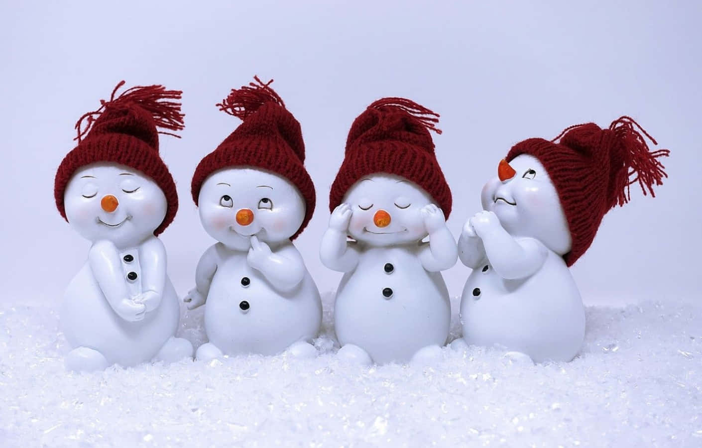 壁紙 — 四個戴著紅色針織帽的快樂雪人公仔一起坐在柔軟的灰色背景前的蓬鬆白雪中。