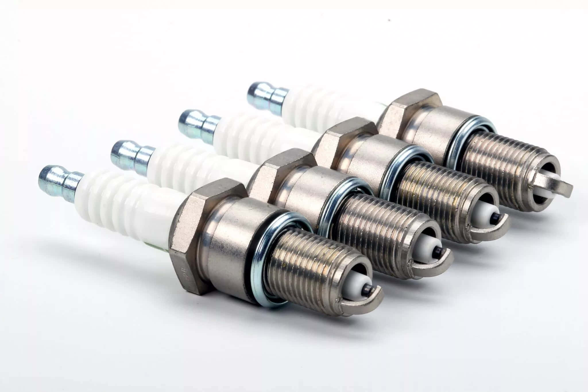 Spark Plug 桌布 壁紙 — 四個新火星塞以對角線排列在潔淨的白色背景上，展示金屬和陶瓷細節。
