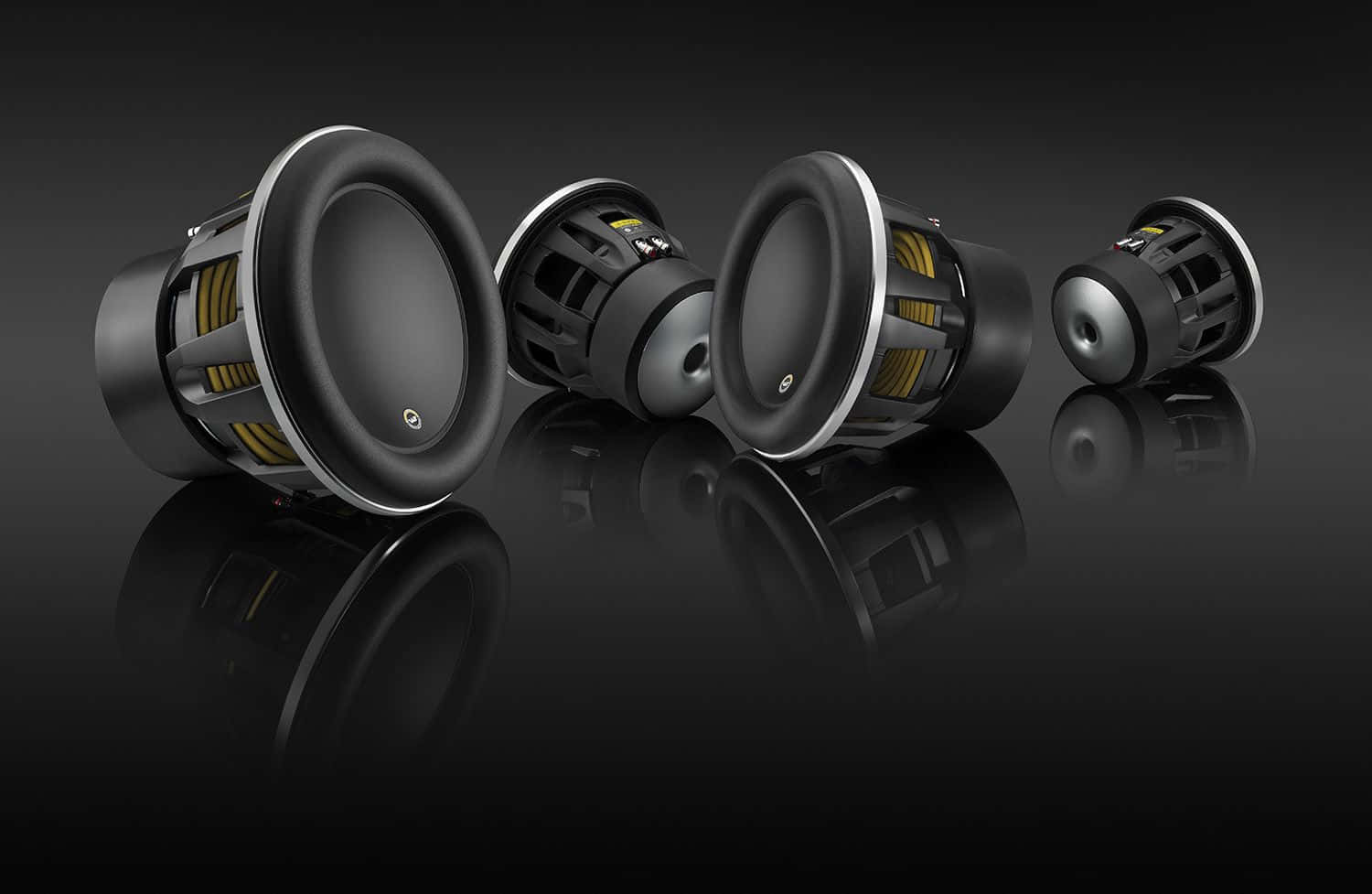 Car Audio 桌布 壁紙 — 四個時尚黑色重低音喇叭，帶有黃色點綴，對角排列在光滑的黑色反光表面上。