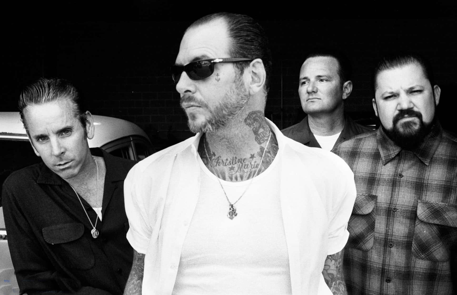 band 桌布 壁紙 — 四個有刺青、表情嚴肅的男人站在一張粗糙的黑白照片中，其中一個戴著太陽眼鏡和白襯衫。