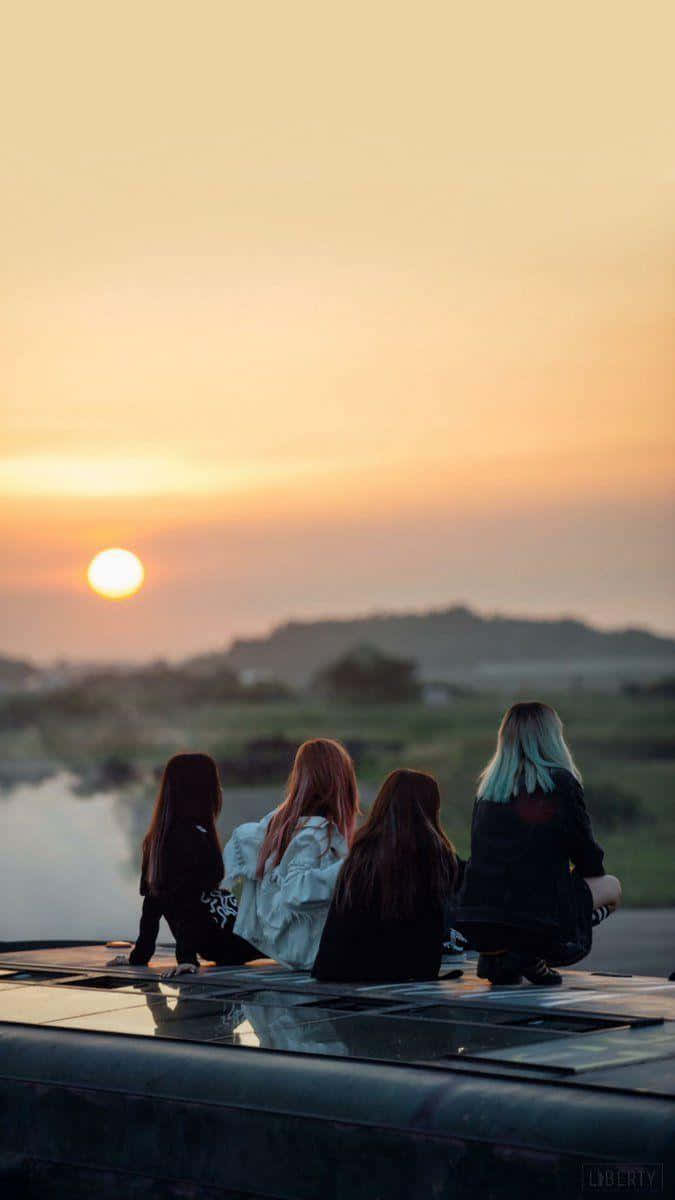 BLACKPINK 桌布 壁紙 — 四個朋友坐在車頂上，看著夕陽落在平靜的湖面和遠處的山丘上。