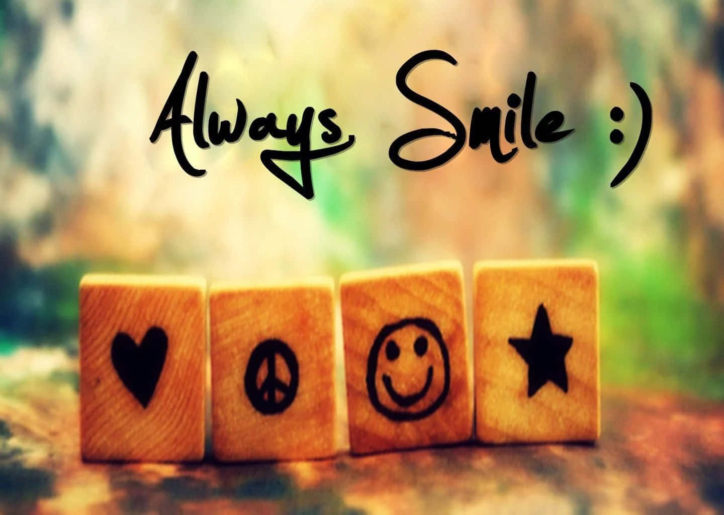 Smile 桌布 壁紙 — 四個木塊上帶有心形、和平、笑臉和星星符號，在柔和模糊的背景上展示手寫訊息 'Always Smile :)'。