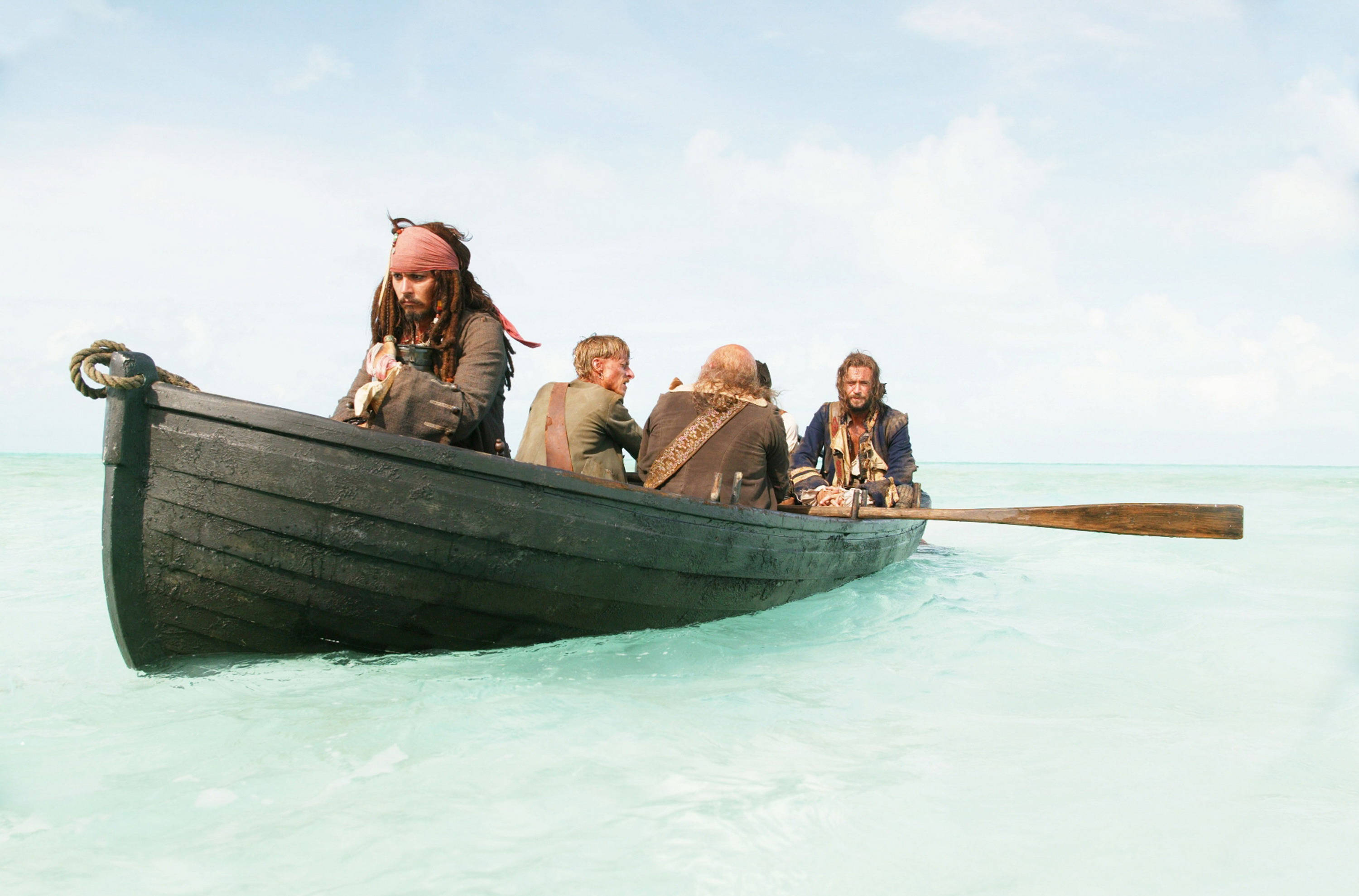Pirates Of The Caribbean 桌布 壁紙 — 四個海盜在一艘破舊的划艇上，在晴朗的藍天下，在平靜的碧綠水面上滑行。