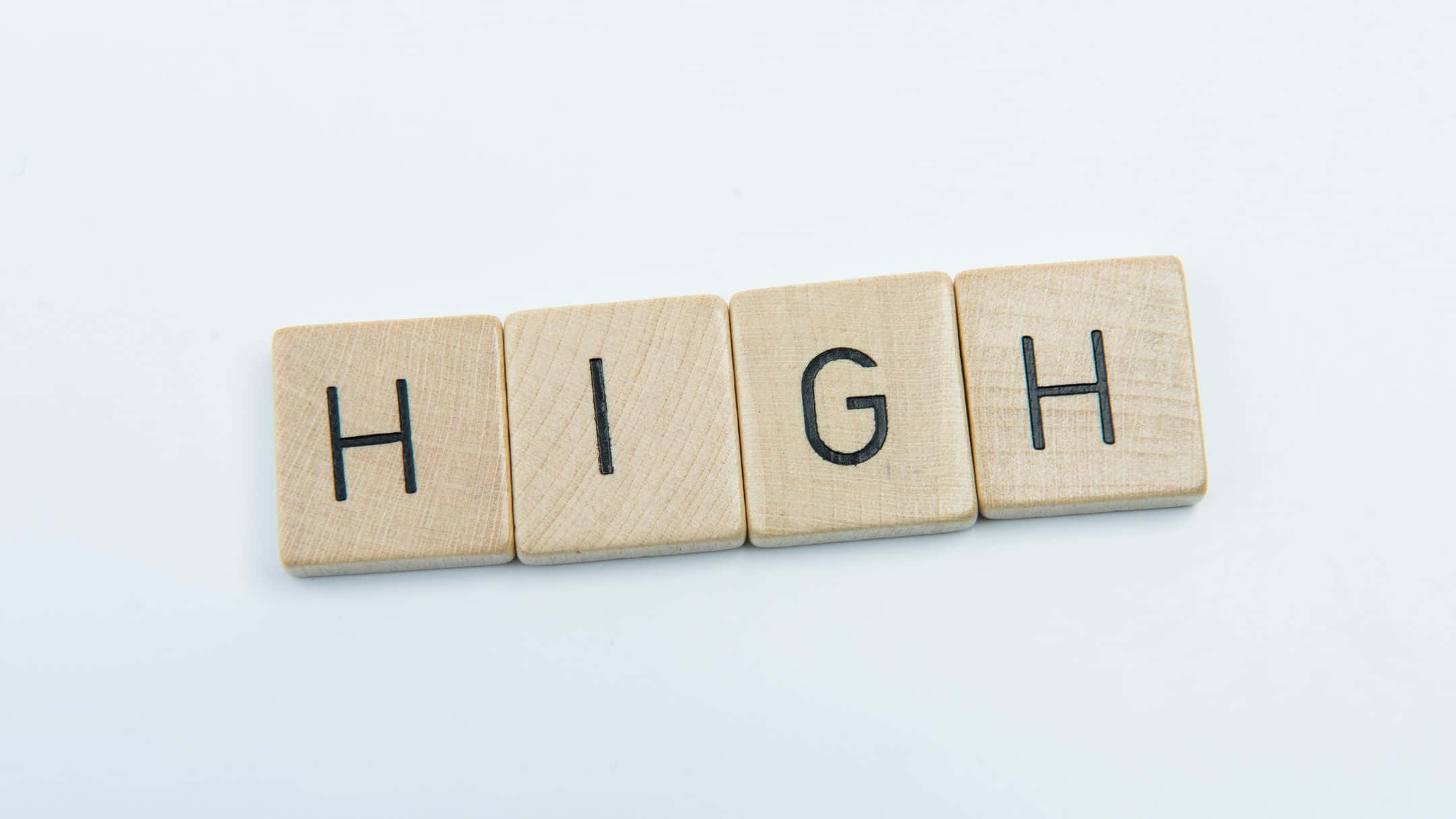 high 桌布 壁紙 — 四個淺色木塊在潔白背景上用粗體黑色字母拼出「HIGH」一詞。