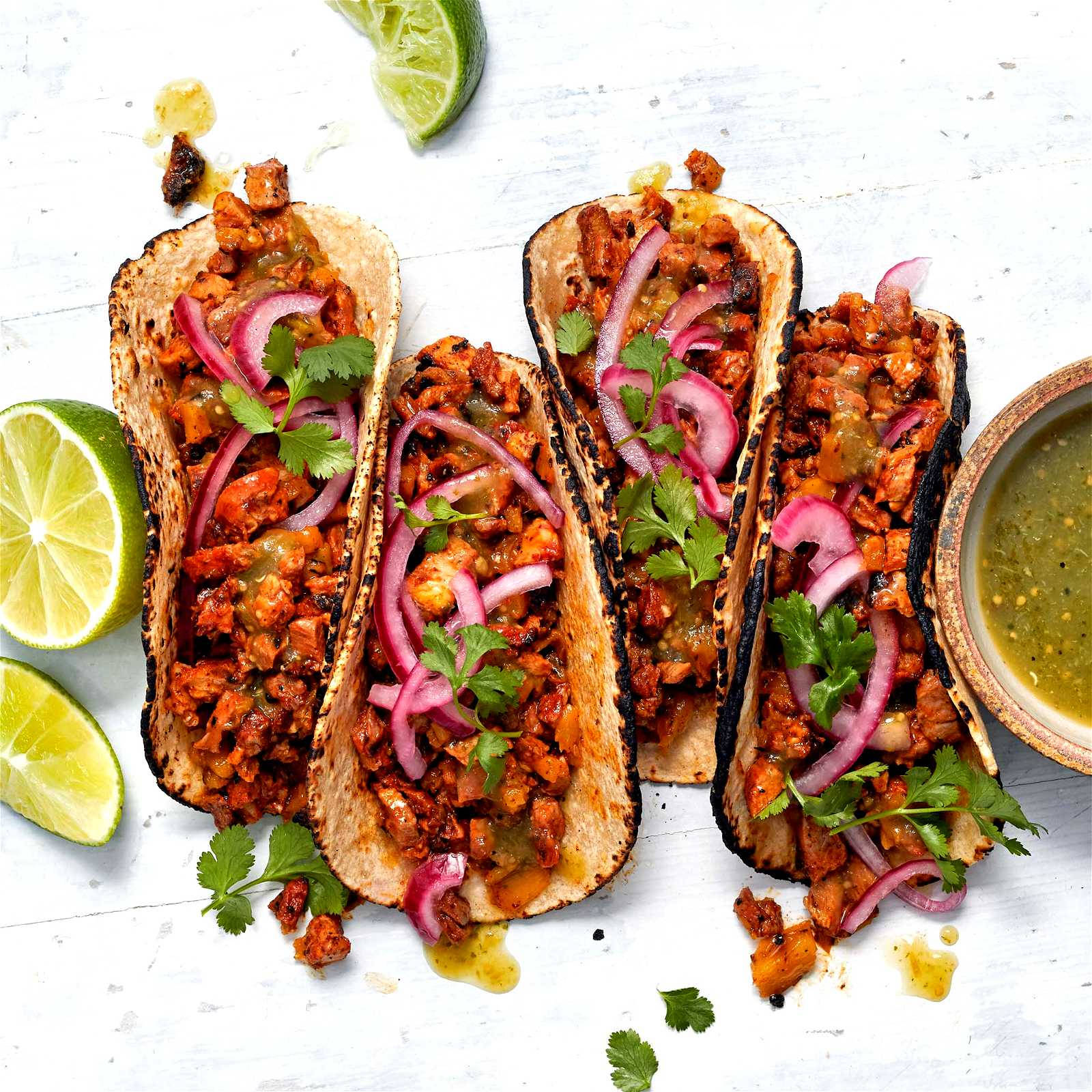 Tacos 桌布 壁紙 — 四個烤雞肉玉米餅，上面放有醃紅洋蔥、香菜和醬汁，放在白色木質表面上，旁邊有萊姆角和青莎莎醬。