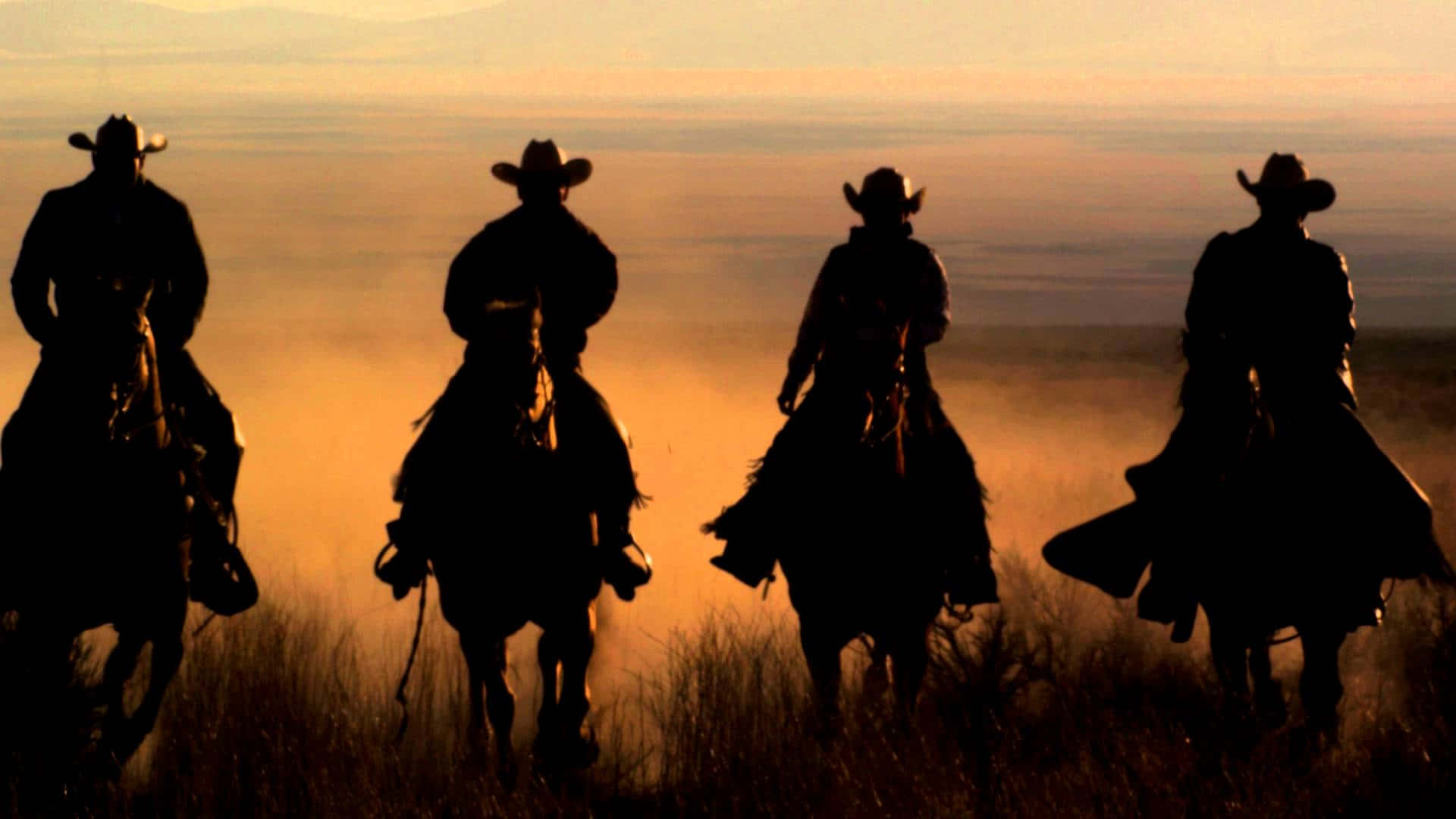 Cowboy 桌布 壁紙 — 四個牛仔騎著馬，在日落時分以剪影形式穿過金色的草原。