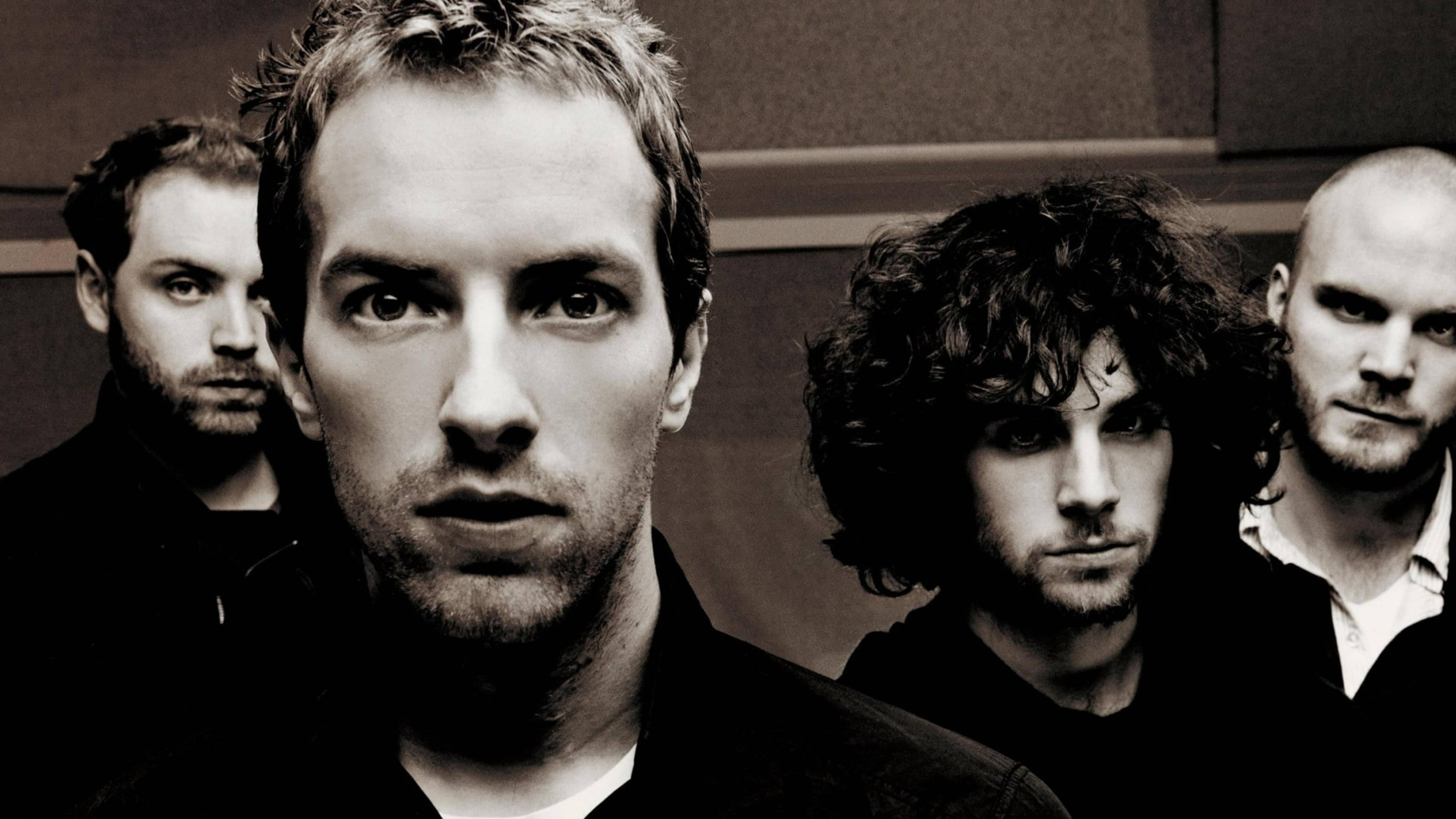 Chris Martin 桌布 壁紙 — 四個男人在黑白鮮明的肖像照中，以強烈的眼神凝視著樸素的牆壁。