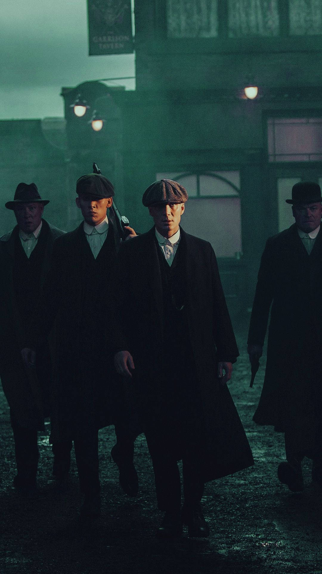 四個穿著風衣和扁帽的男人在夜晚霧濛濛的城市街道上行走。 — Peaky Blinders 壁紙