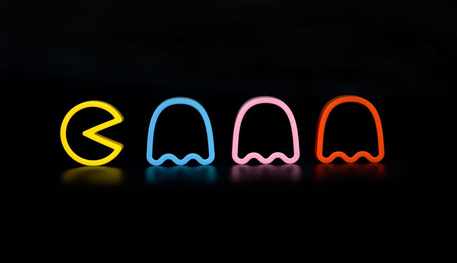 電玩遊戲 桌布 壁紙 — 四個發光的 Pac-Man 角色，分別為黃色、藍色、粉紅色和橙色，站在帶有柔和反射的黑色背景前。