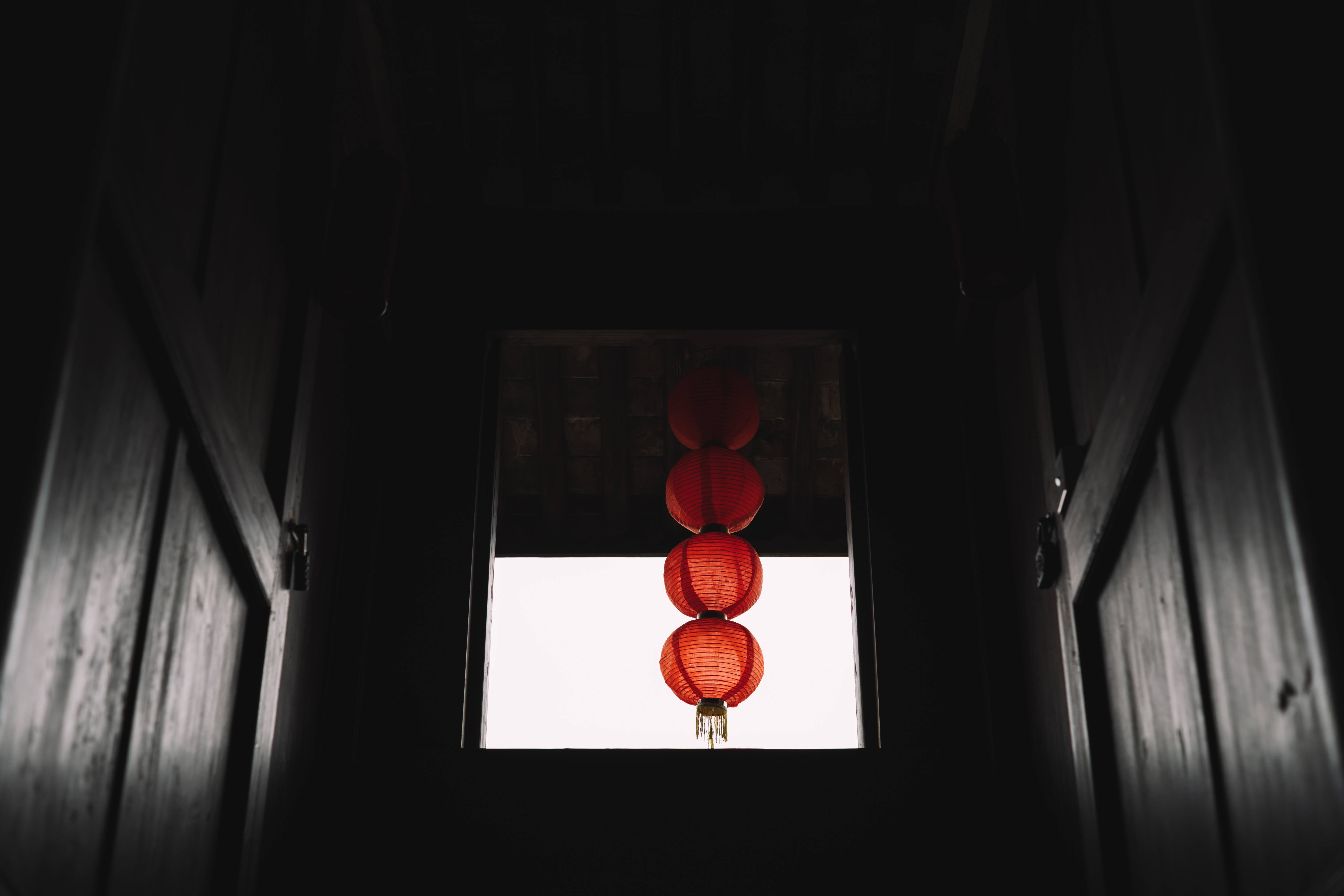 中文 桌布 壁紙 — 四個發光的紅色紙燈籠垂直懸掛在一個明亮的窗戶前，窗戶由深色木樑框著。