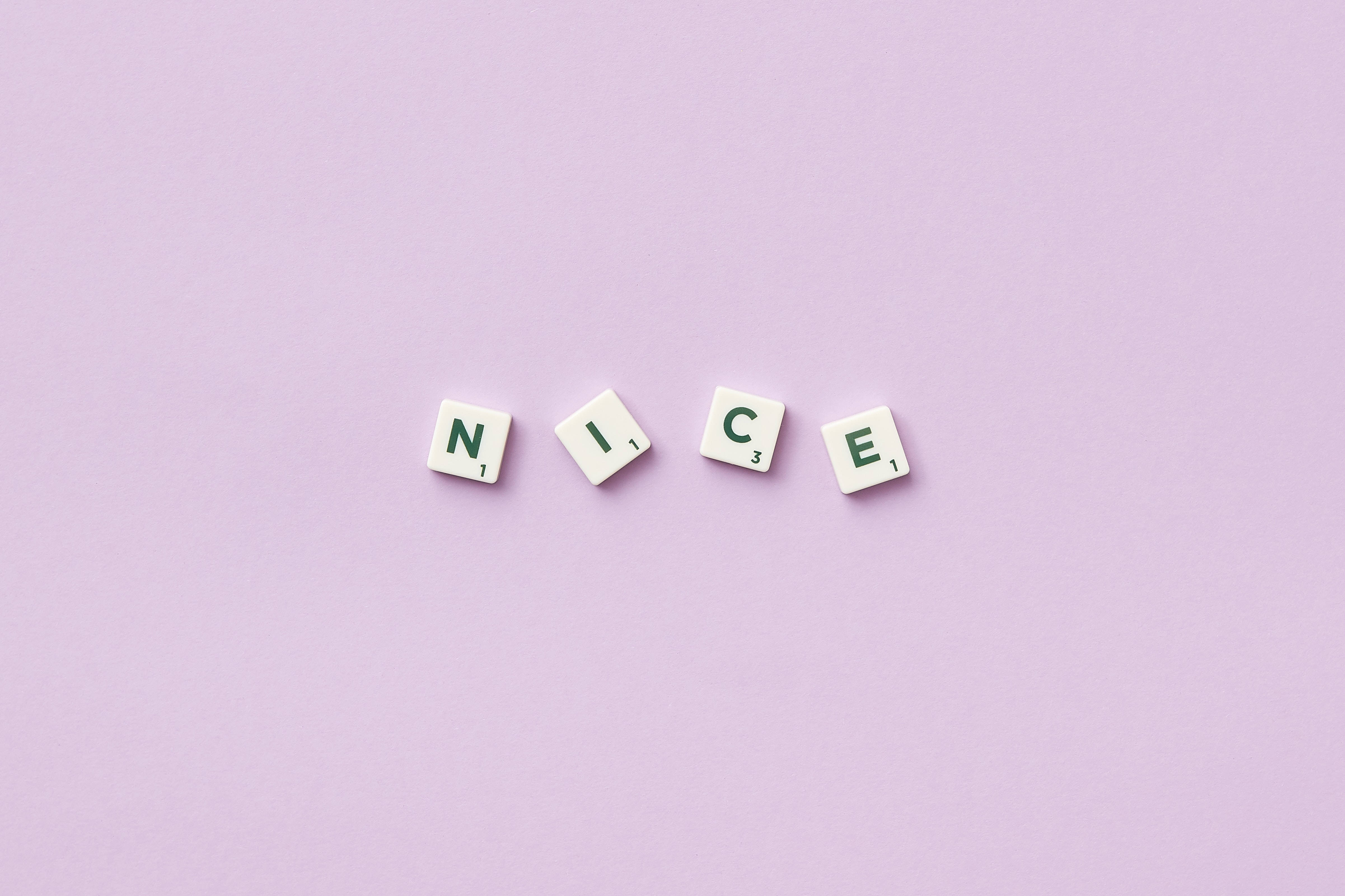 可愛粉彩風格 桌布 壁紙 — 四個白色 Scrabble 字塊拼出綠色字母 'NICE'，放置在柔和的薰衣草背景上。