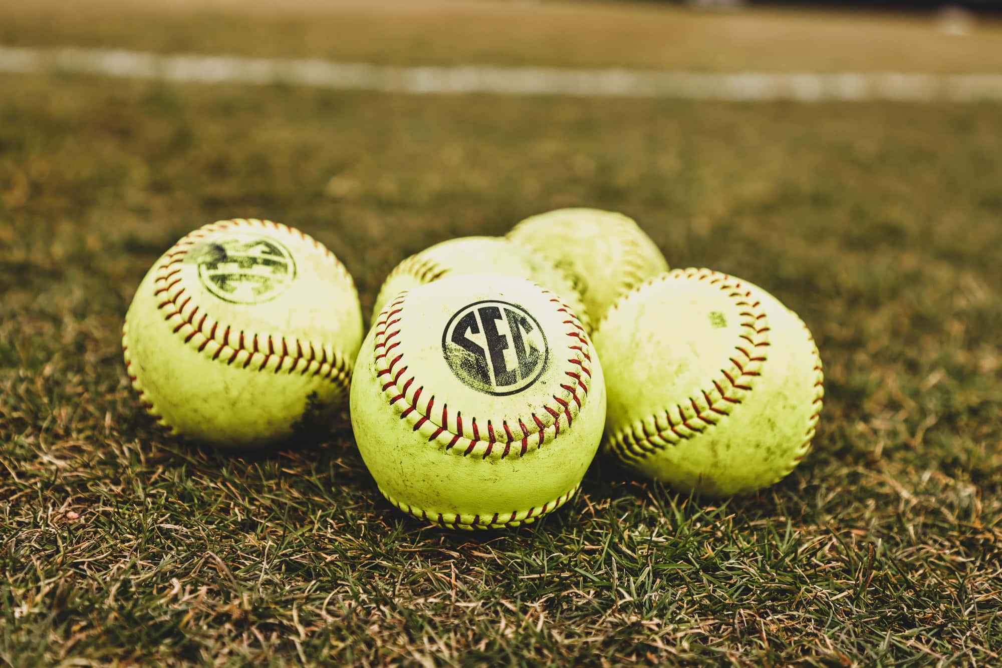Softball 桌布 壁紙 — 四個磨損的壘球，帶有紅色縫線，在溫暖的陽光下躺在草地上。