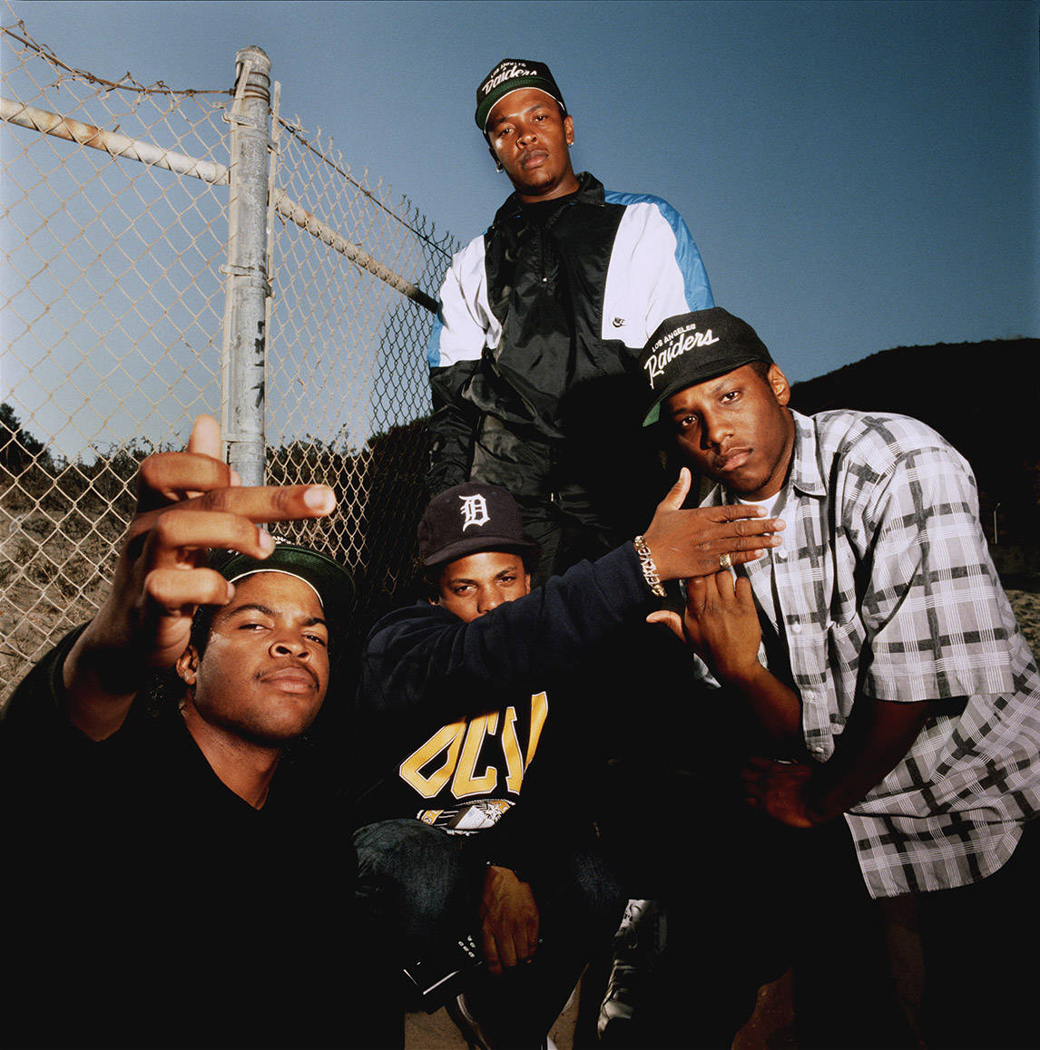 Ice Cube 桌布 壁紙 — 四個穿著90年代街頭服飾的男人在晴朗藍天下自信地靠在鐵絲網圍欄上擺姿勢。