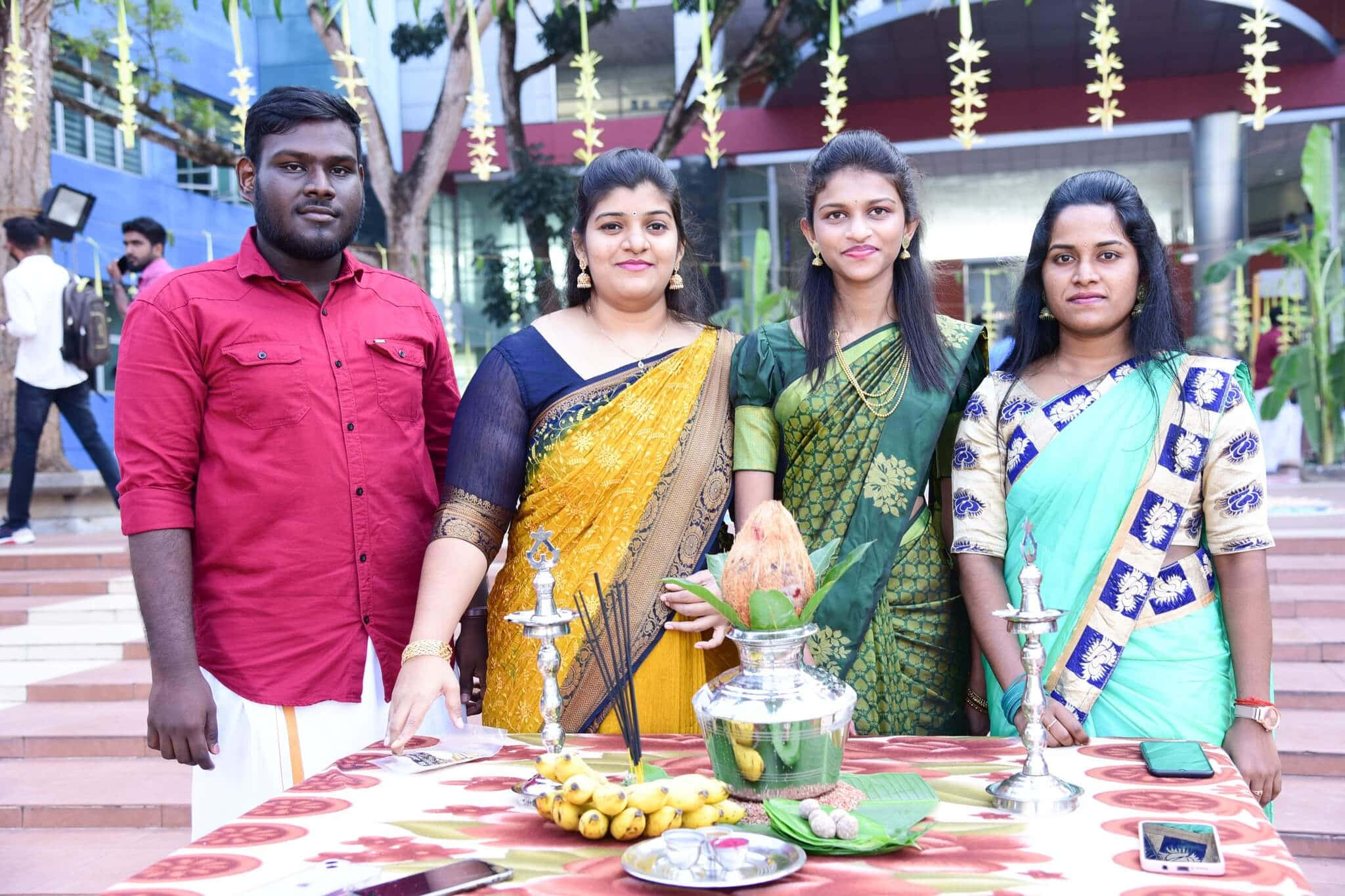 Pongal 桌布 壁紙 — 四個穿著傳統印度服飾的人站在一個裝飾過的桌子後面，桌子上有祭品，在戶外的文化儀式中進行。