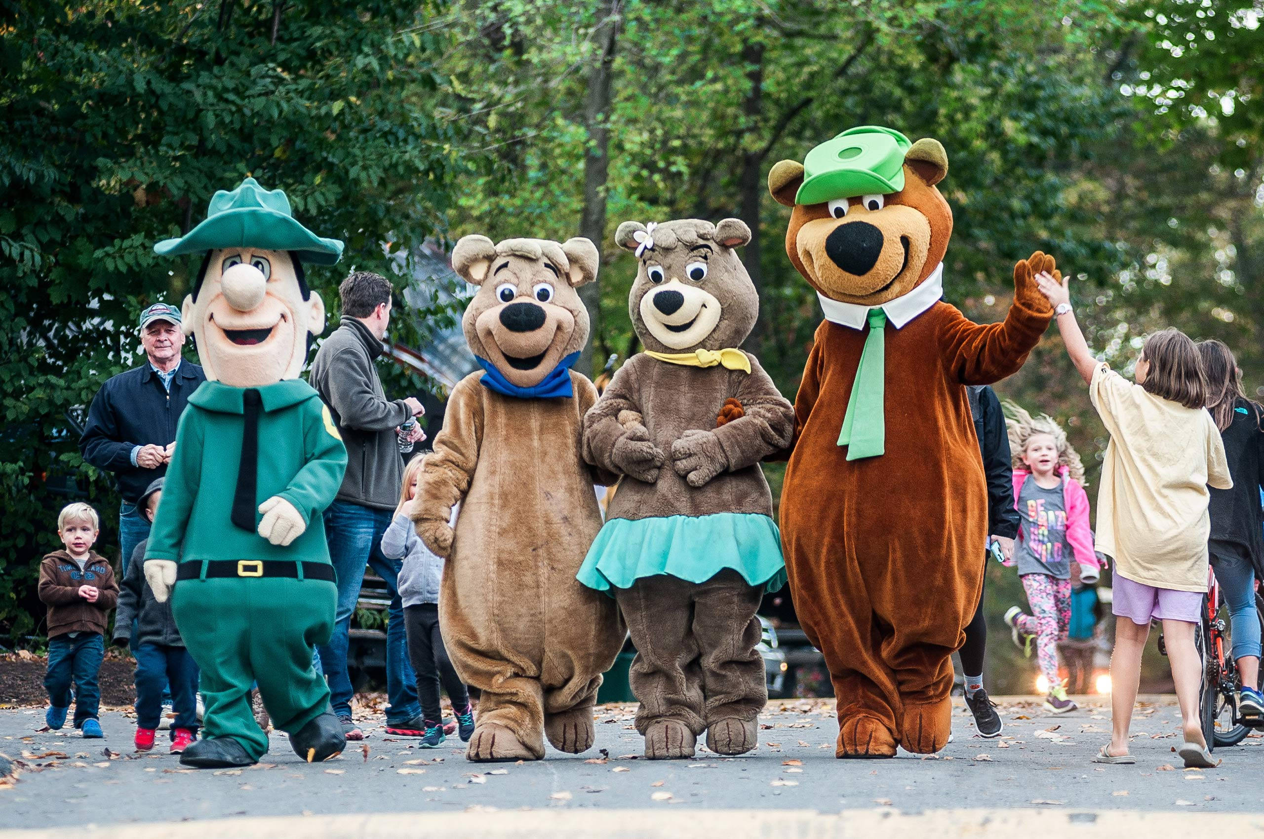 Yogi 桌布 壁紙 — 四個穿著服裝的快樂卡通熊角色在綠葉成蔭的公園裡與孩子們互動。
