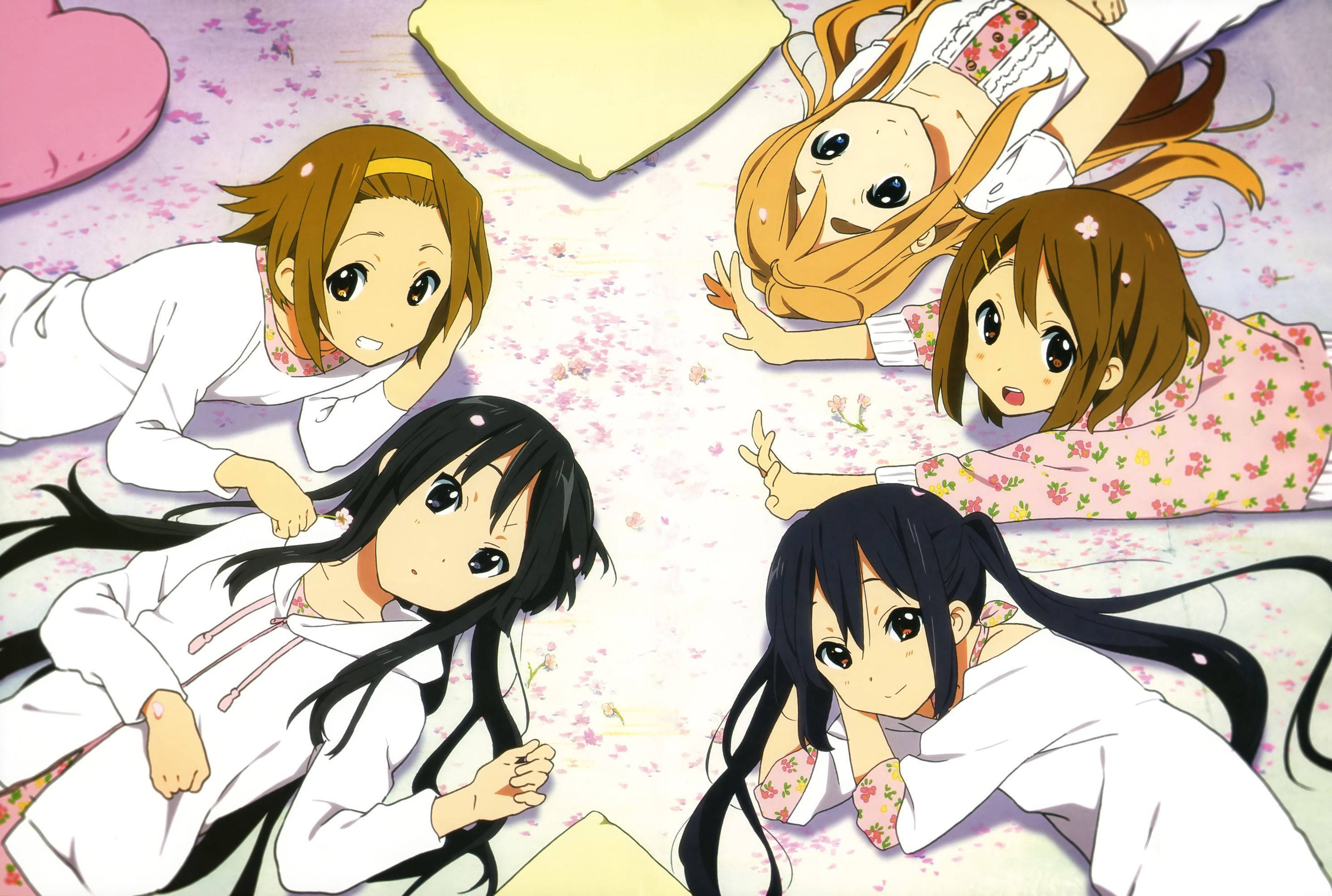 K-on 桌布 壁紙 — 四個穿著睡衣的動漫女孩躺在散落著粉紅色櫻花的地板上，微笑著擺出俏皮的姿勢。
