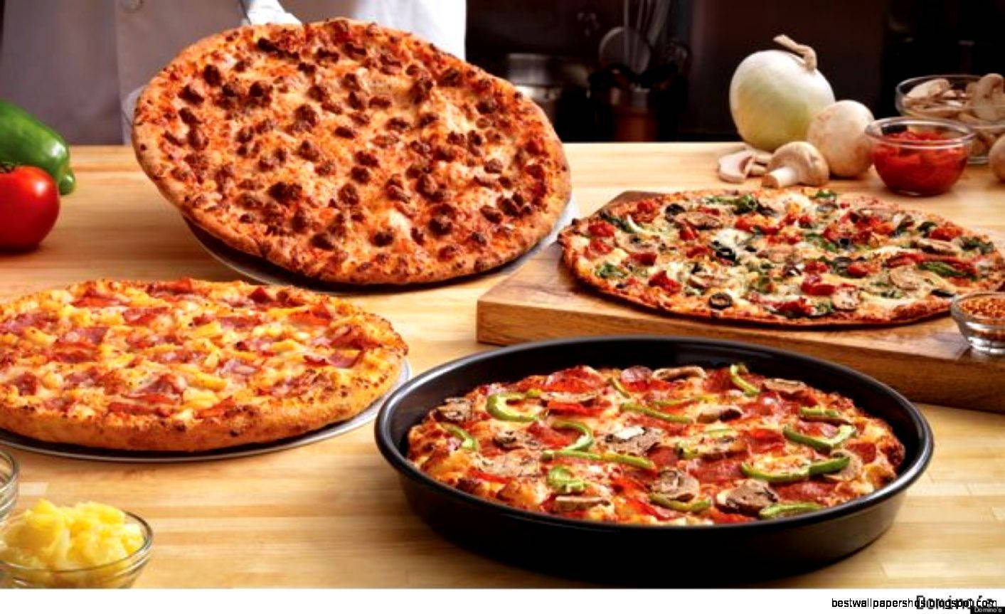 Dominos Pizza 桌布 壁紙 — 四個美味配料的披薩誘人地放在木桌上，周圍是新鮮食材。