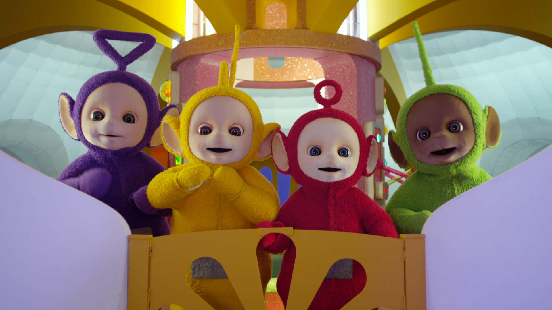 Teletubbies 桌布 壁紙 — 四個色彩繽紛的Teletubbies穿著紫色、黃色、紅色和綠色的服裝，在明亮的黃色車輛內微笑。