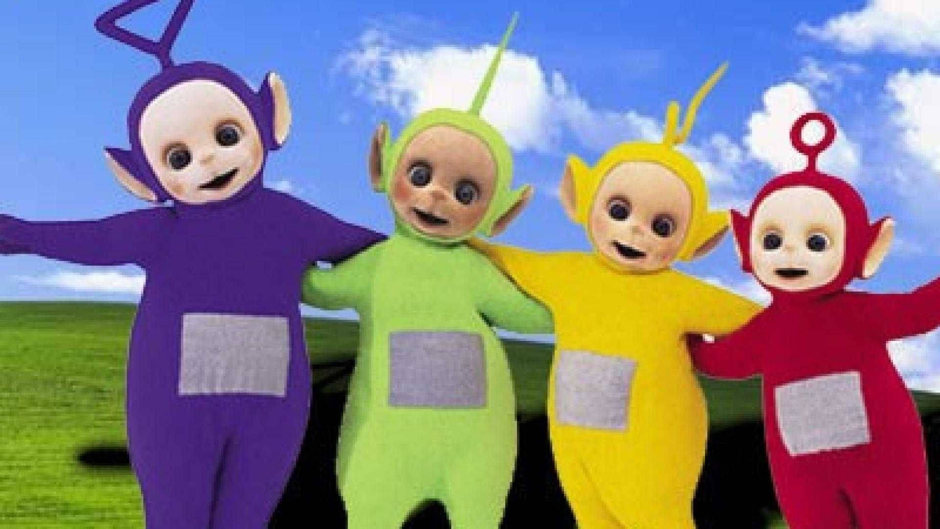 Cartoon 桌布 壁紙 — 四個色彩繽紛的Teletubbies，分別是紫色、綠色、黃色和紅色，在一片草地上手挽手站著，背景是晴朗的藍天和 fluffy 白雲。