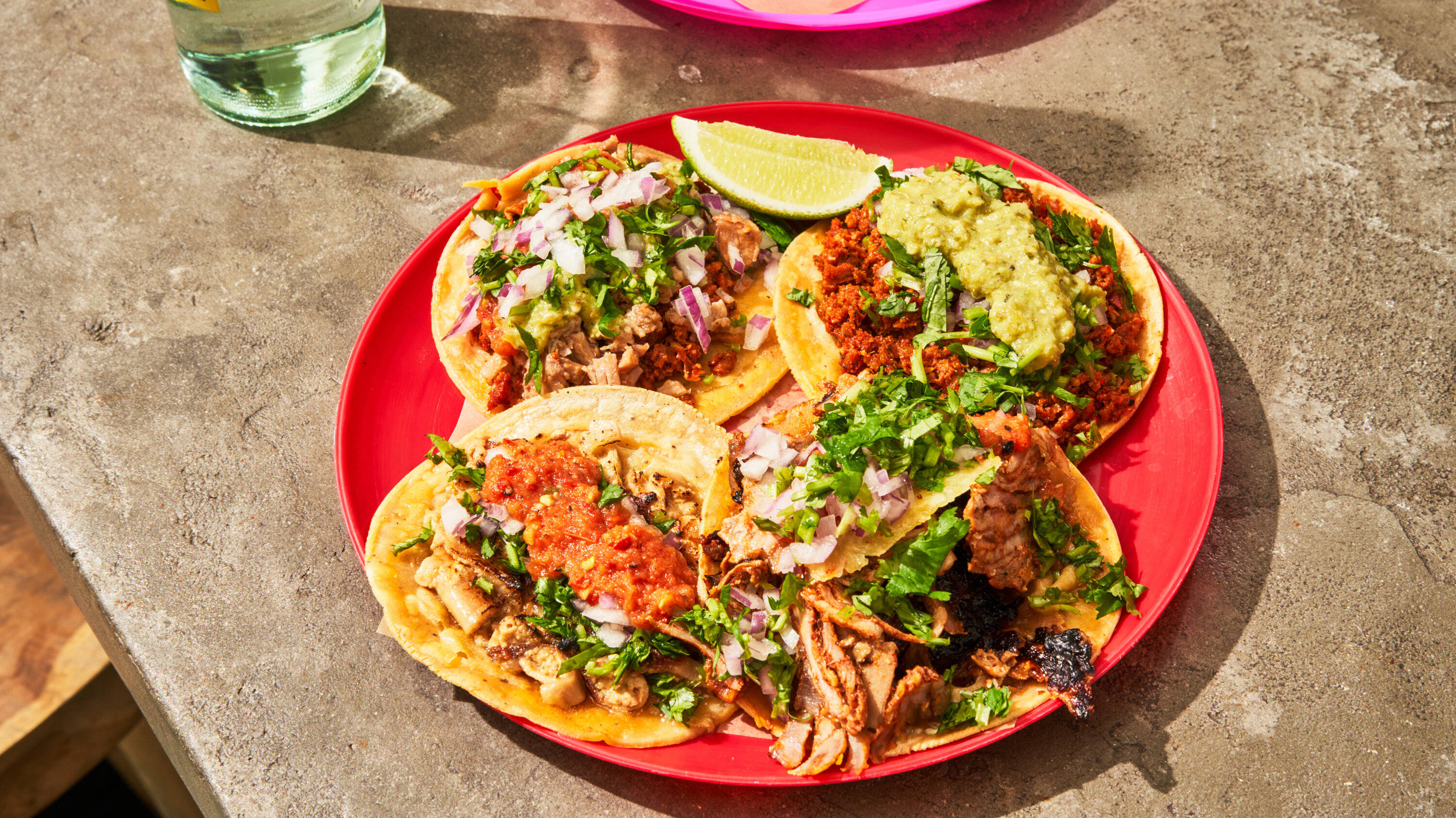 Mexican Food 桌布 壁紙 — 四個色彩繽紛的墨西哥捲餅配酪梨醬和莎莎醬，放在鮮紅色盤子上，在混凝土桌上溫暖陽光下。