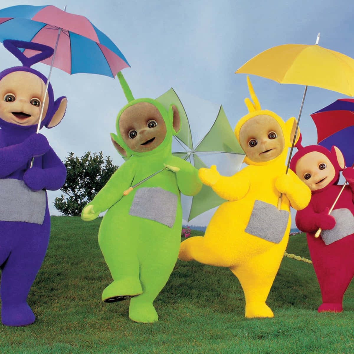 Teletubbies 桌布 壁紙 — 四個色彩繽紛的天線寶寶在晴朗的藍天下，在草地山坡上開心地撐著傘。
